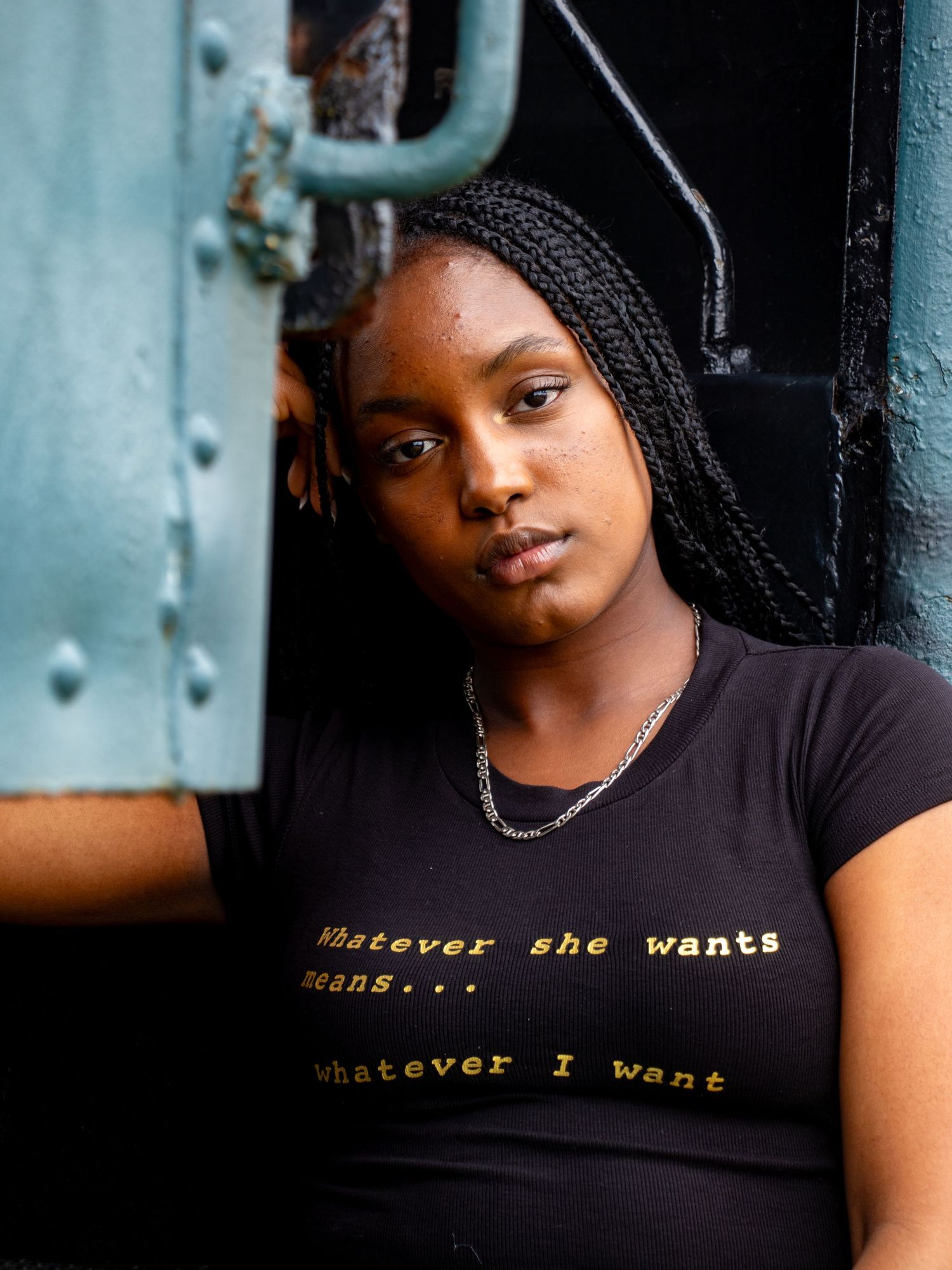 Woman in black graphic crop tee leaning against metal door.