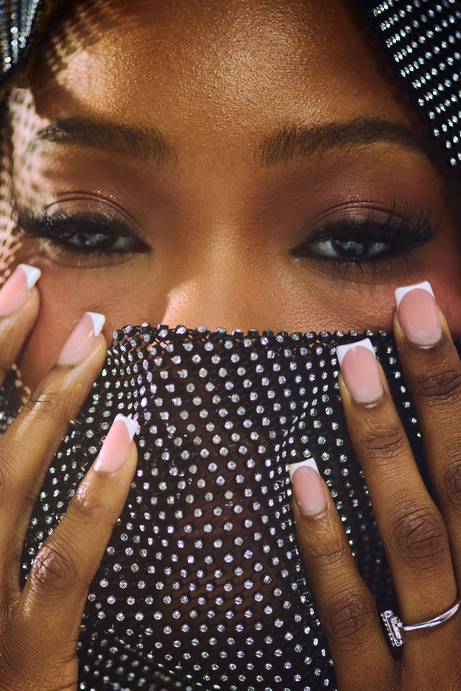 Close-up of a Black woman with long lashes holding a sparkly black polka-dot veil over her face.