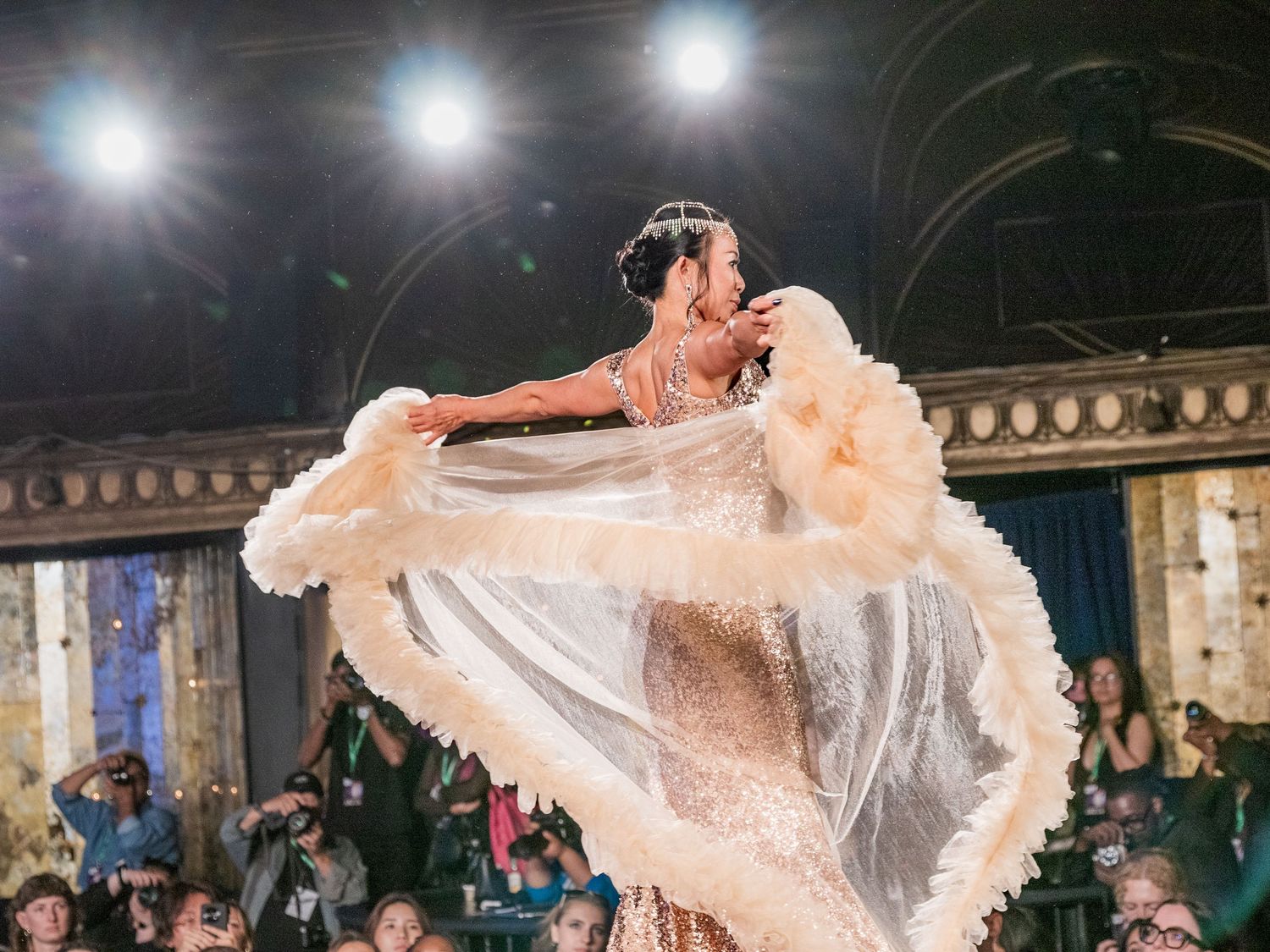 Model showcases flowing white feather and tulle bridal gown on dramatic fashion runway.