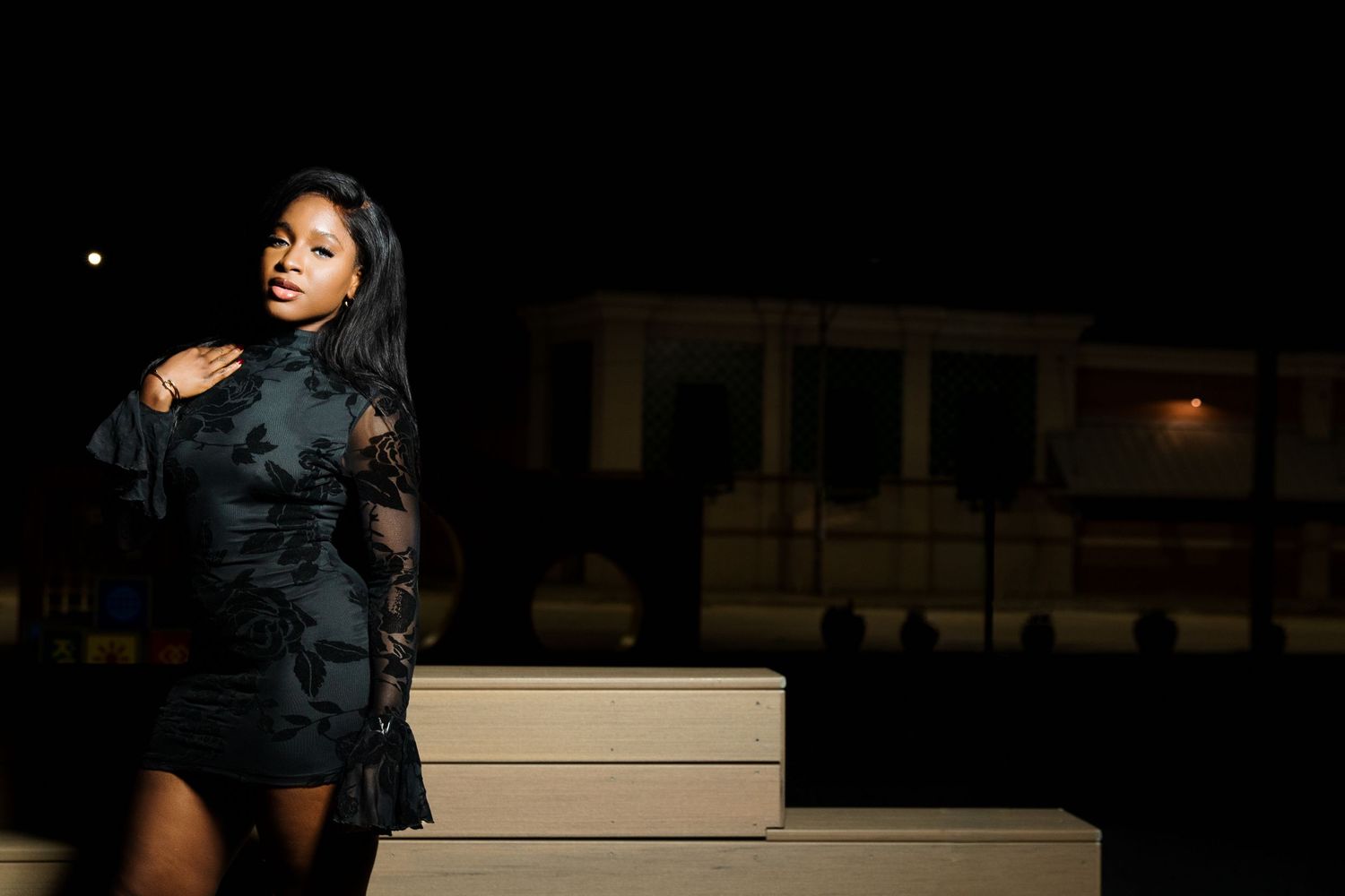 Woman in black lace mini dress poses on steps at night.