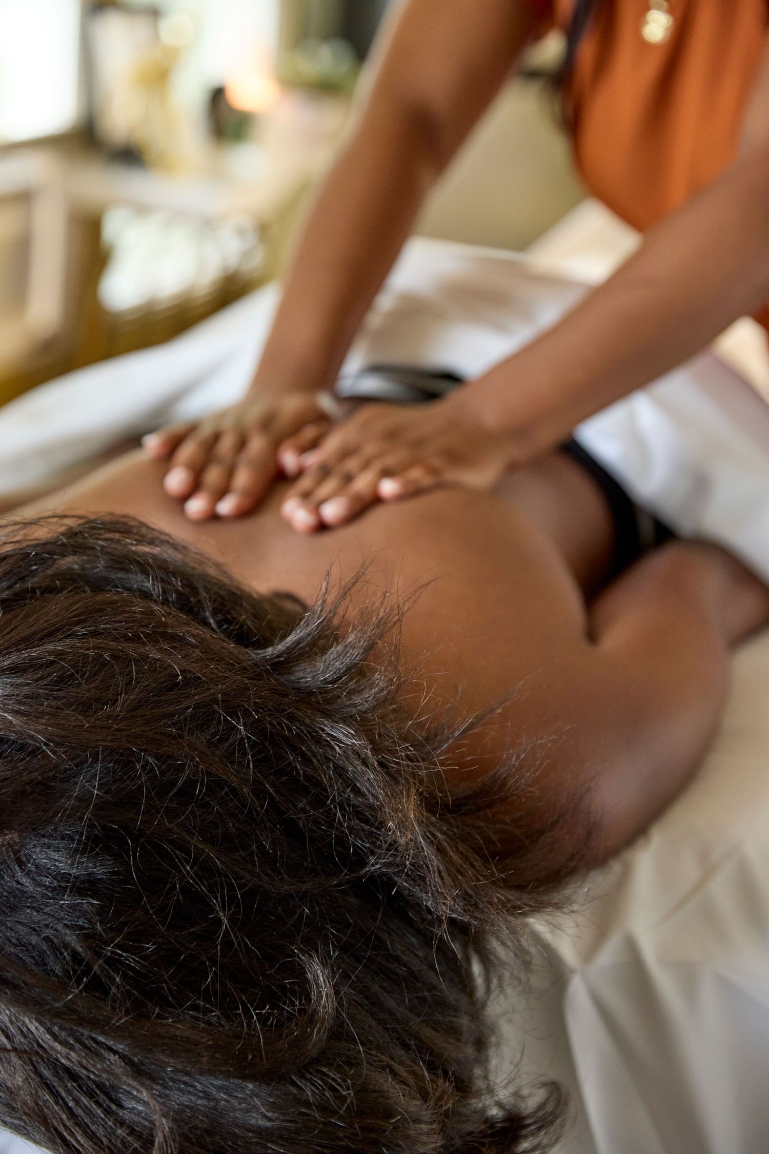 A massage therapist in an orange top performs a relaxing back massage on a client lying on a white table.