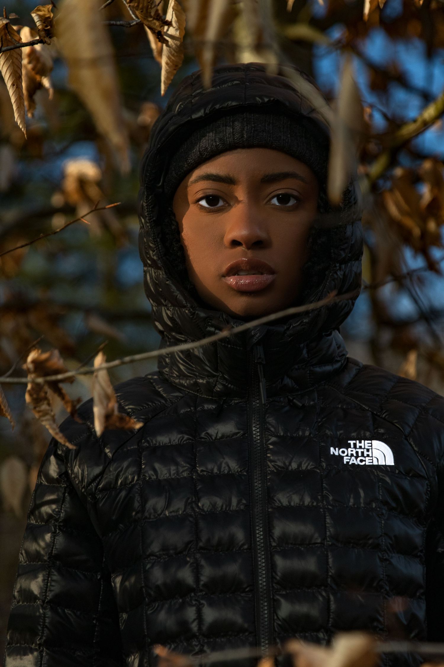 Young woman in black North Face hooded jacket and beanie surrounded by winter branches.
