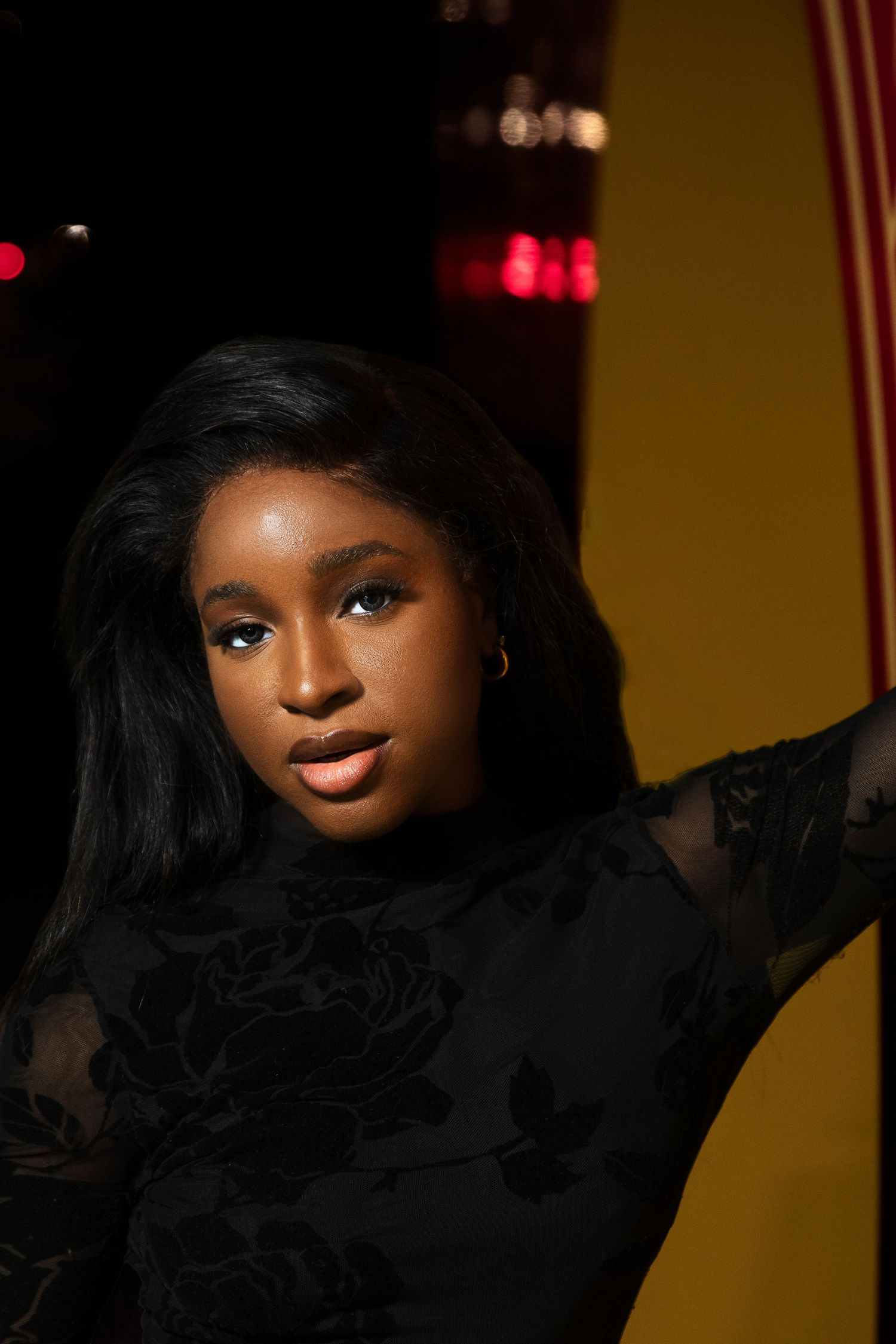 Beautiful young Black woman with straight hair wearing a black floral dress in warm lighting.