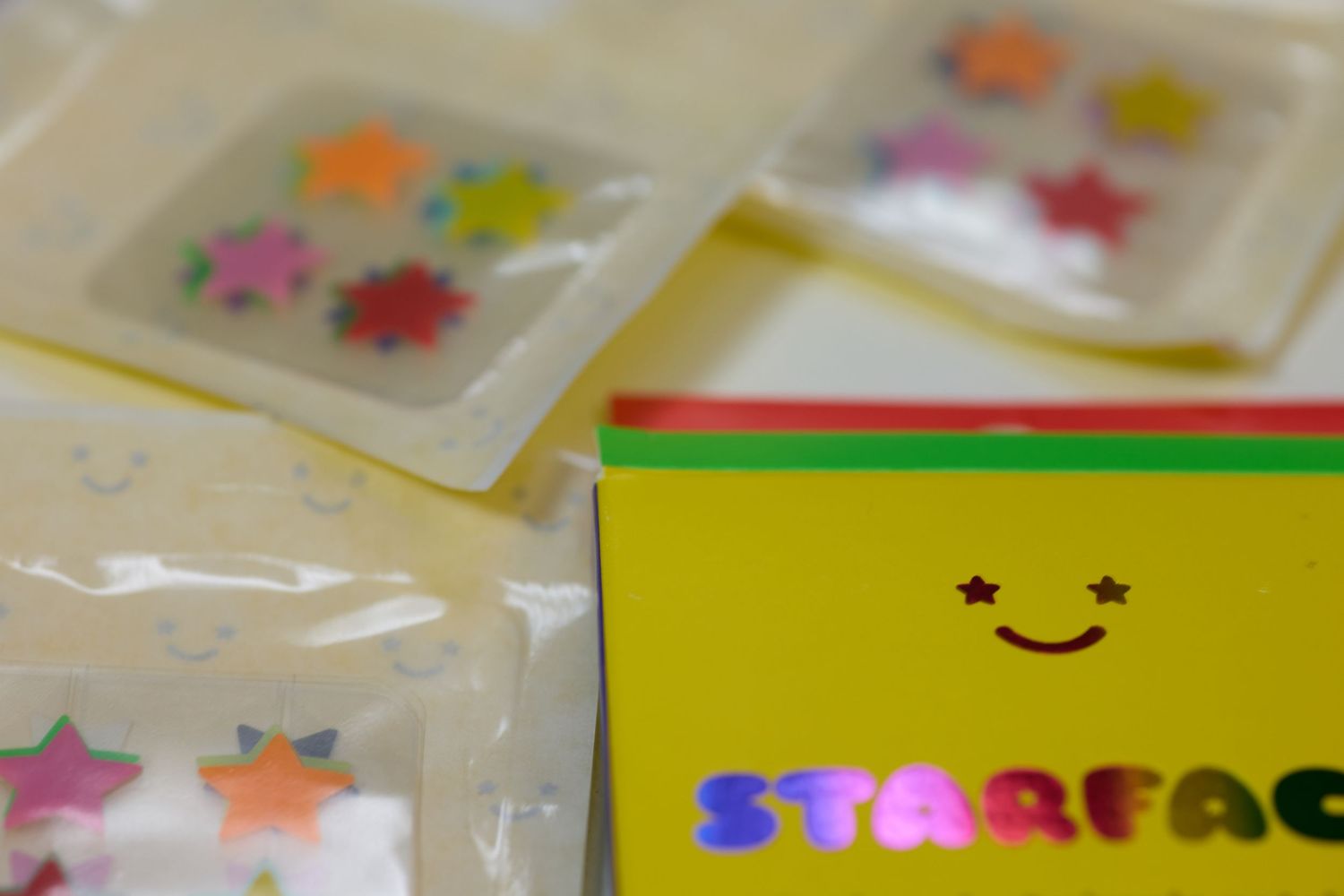 Starface hydro-star pimple patches in colorful star shapes displayed in clear packaging next to yellow branded box.