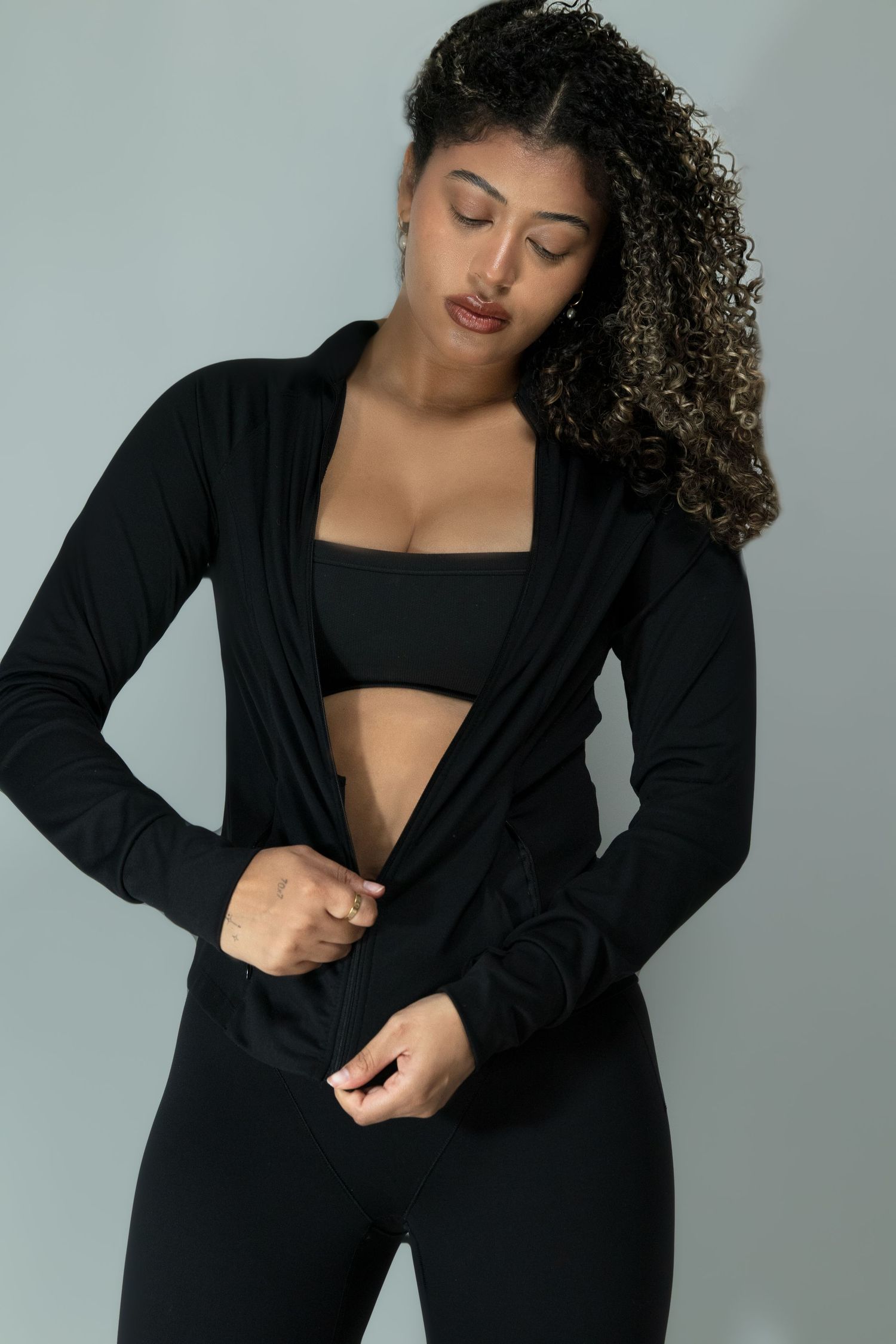 Woman with curly hair wearing black athletic set with open cardigan posing in studio setting.