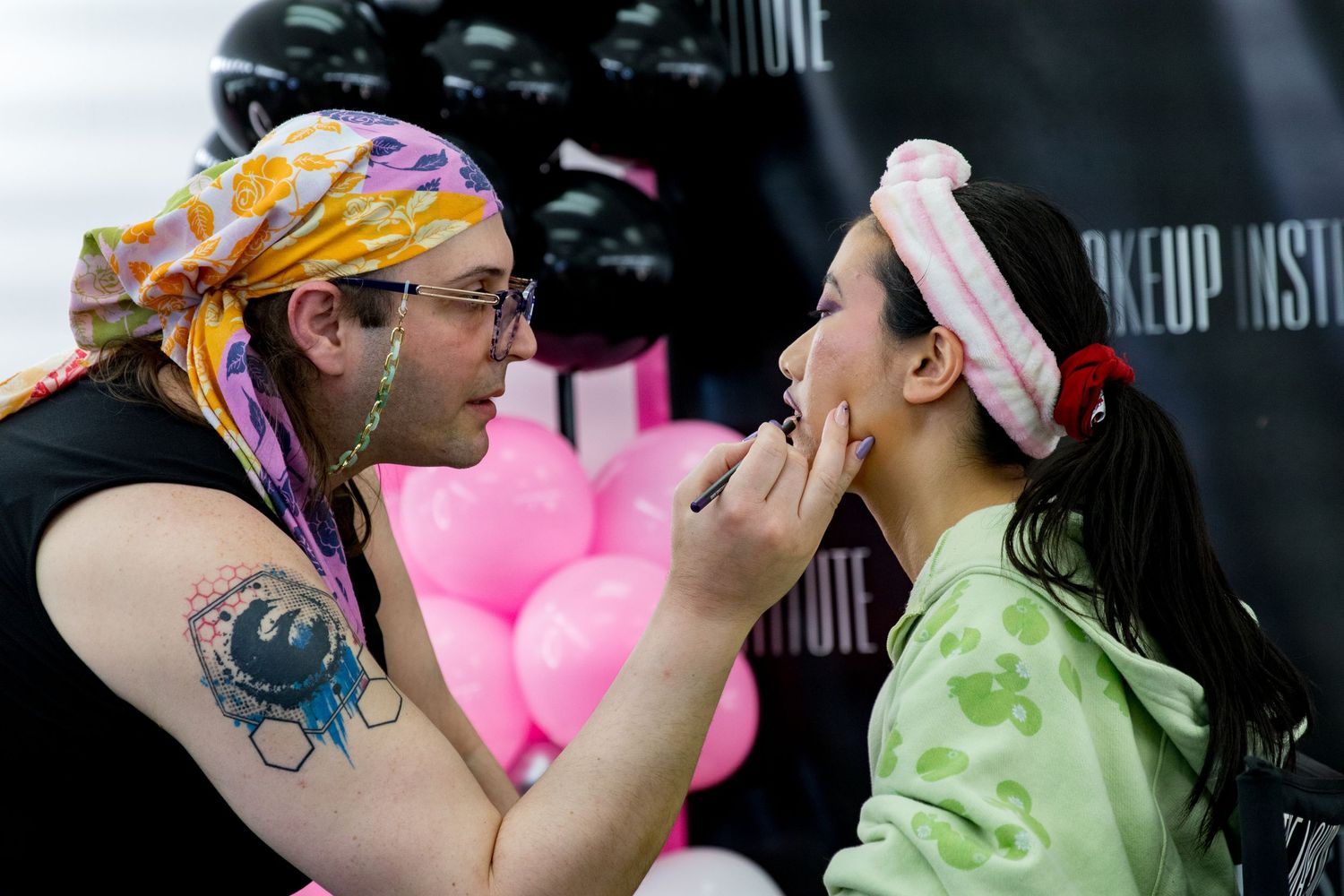 Close-up of a makeup artist carefully applying cosmetics to a young woman's face at a beauty event.