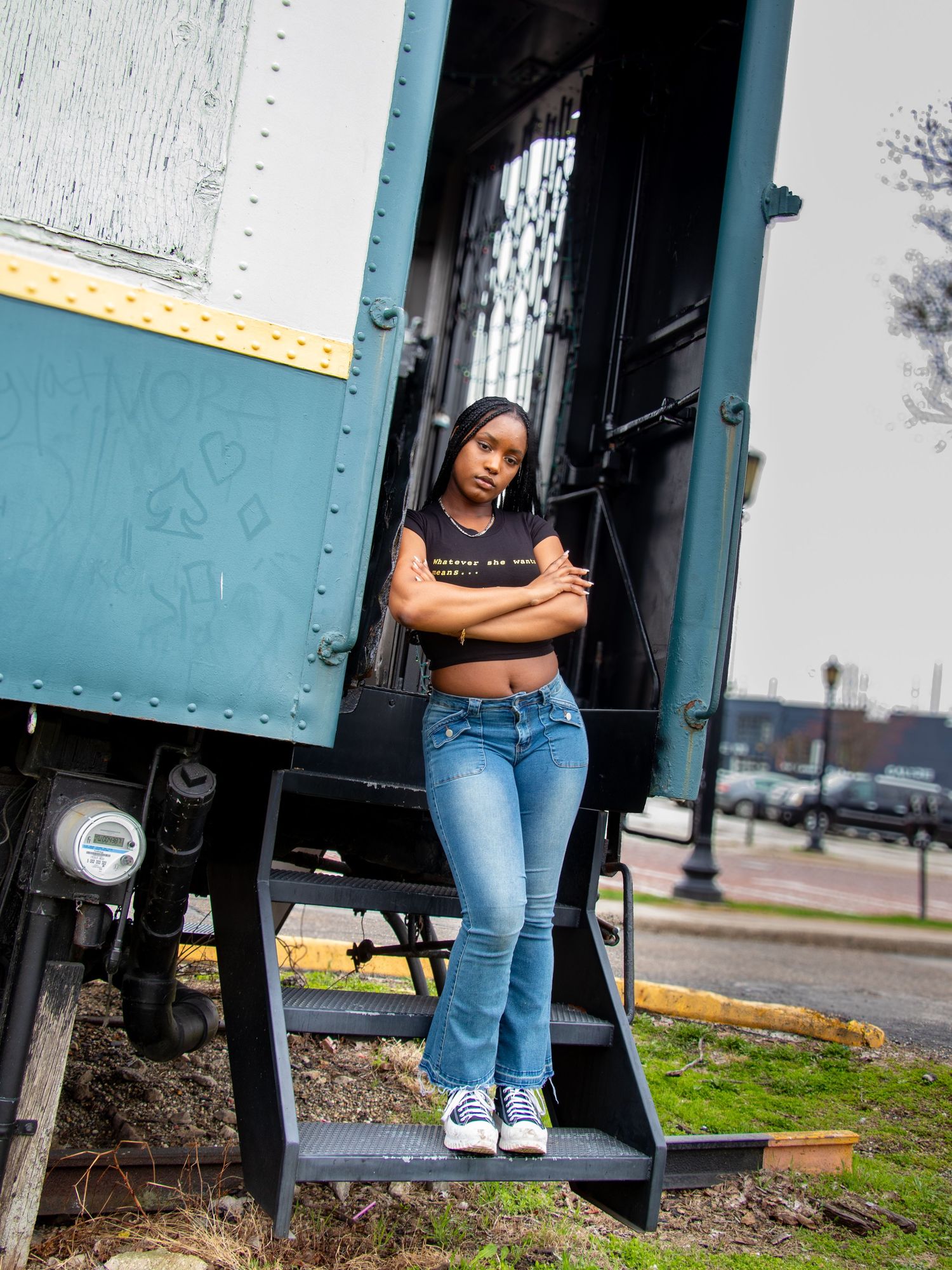 Young woman in crop top and flare jeans standing on train car steps confidently.