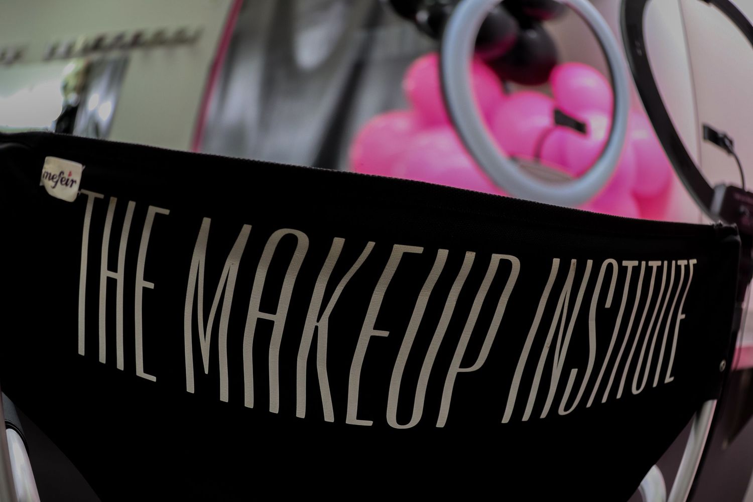Black chair with 'The Makeup Institute' text in gold letters at a professional makeup school.