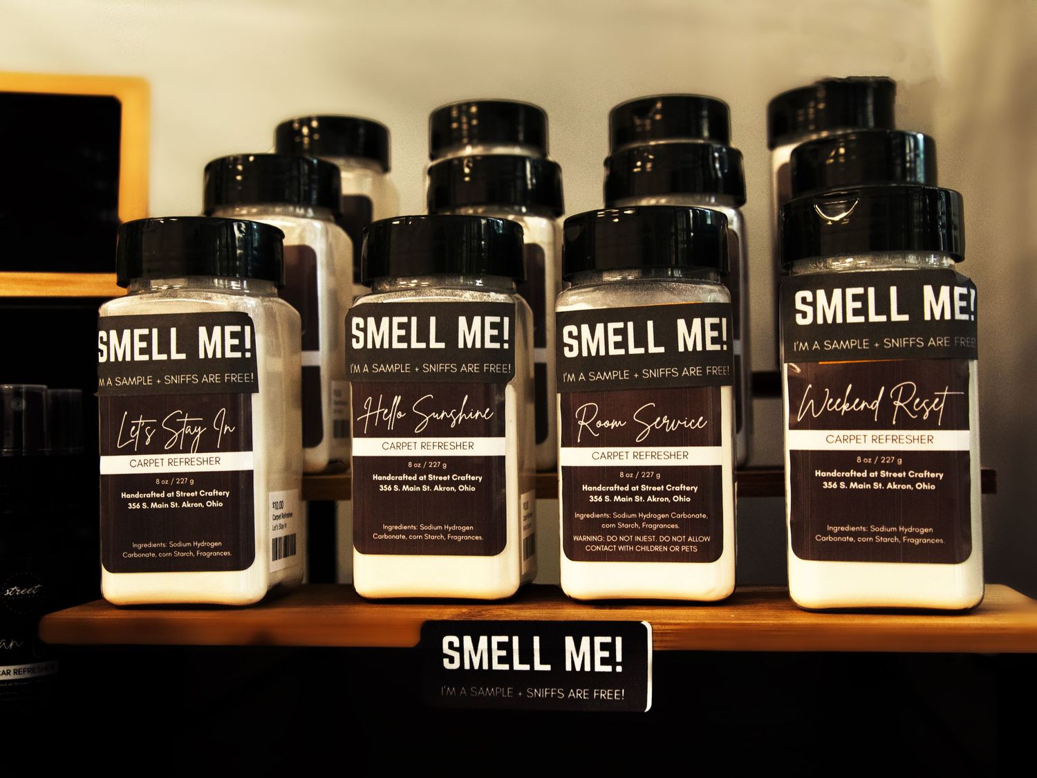 Row of Smell Me scented candle sample shakers on a wooden shelf at Street Craftery store.