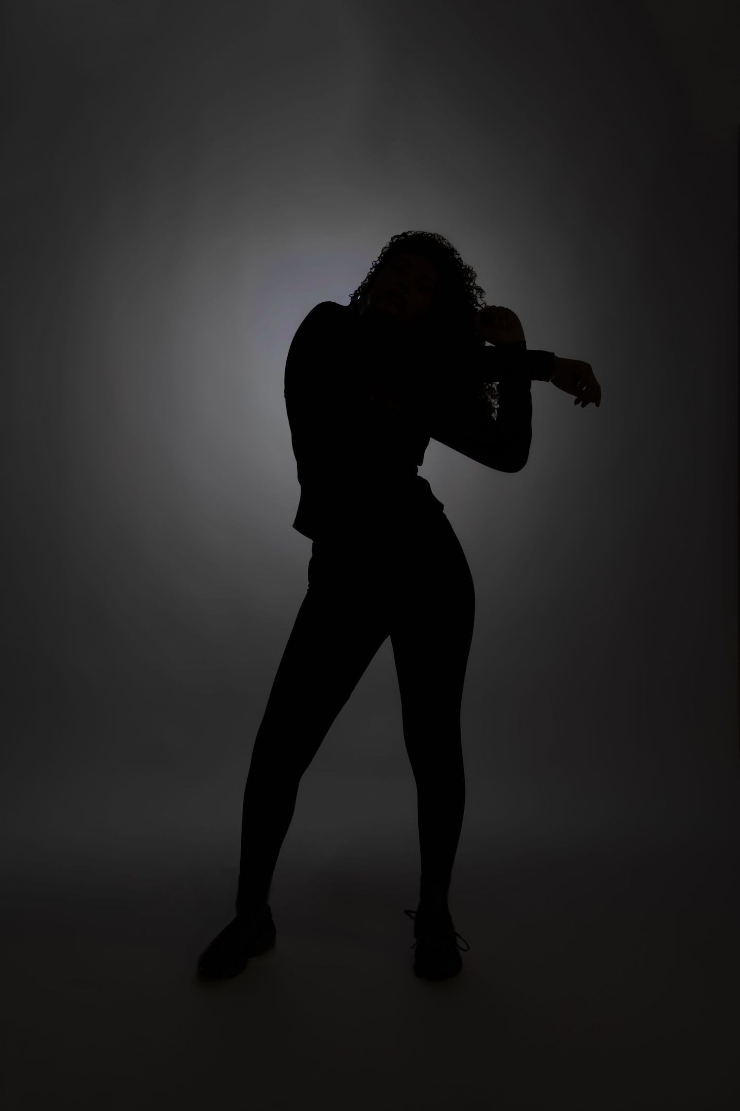 Silhouette of a woman in a dynamic dance pose against a dark background with spotlight.