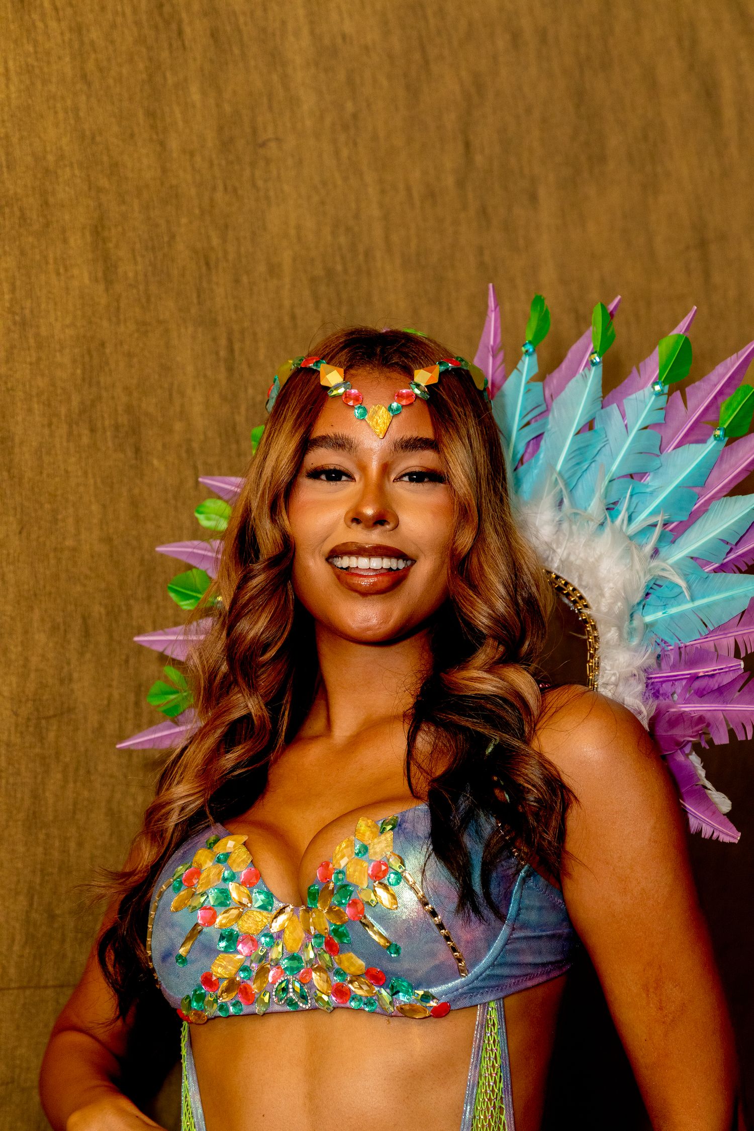 Young woman in vibrant carnival outfit with multicolored feathered wings and jeweled bodice.