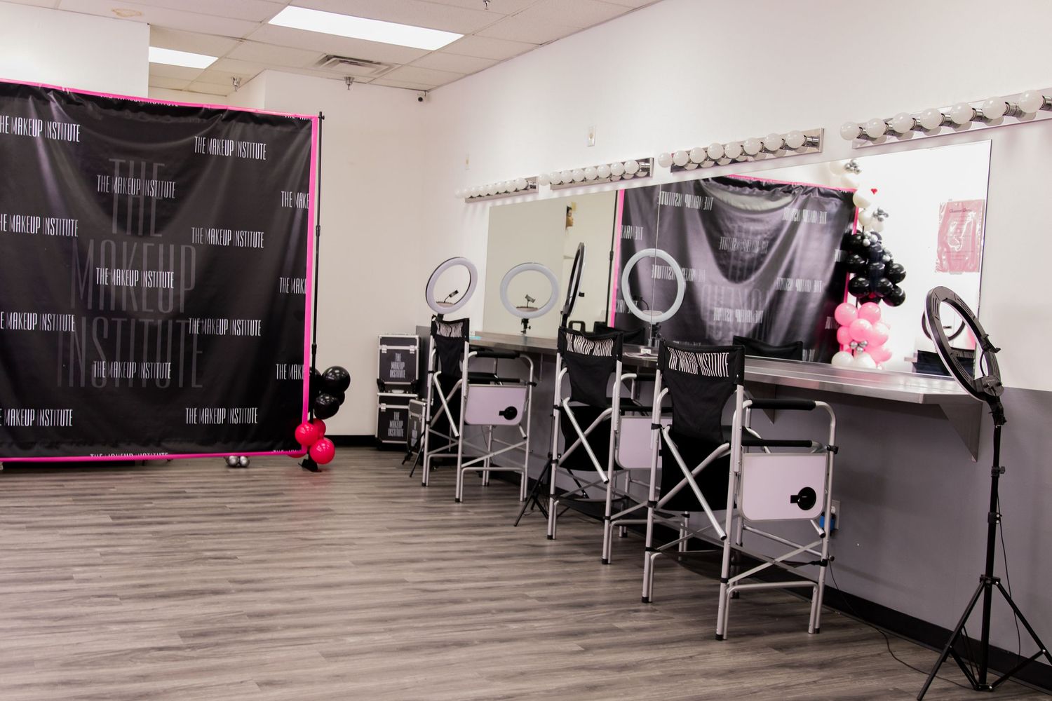 Professional makeup studio with ring lights, black and pink decor, and makeup stations along the wall.