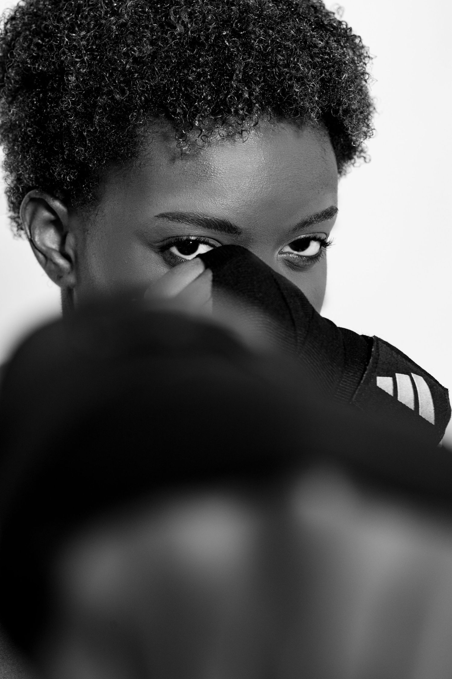 Black and white close-up portrait of a female boxer partially hiding face behind a boxing glove.