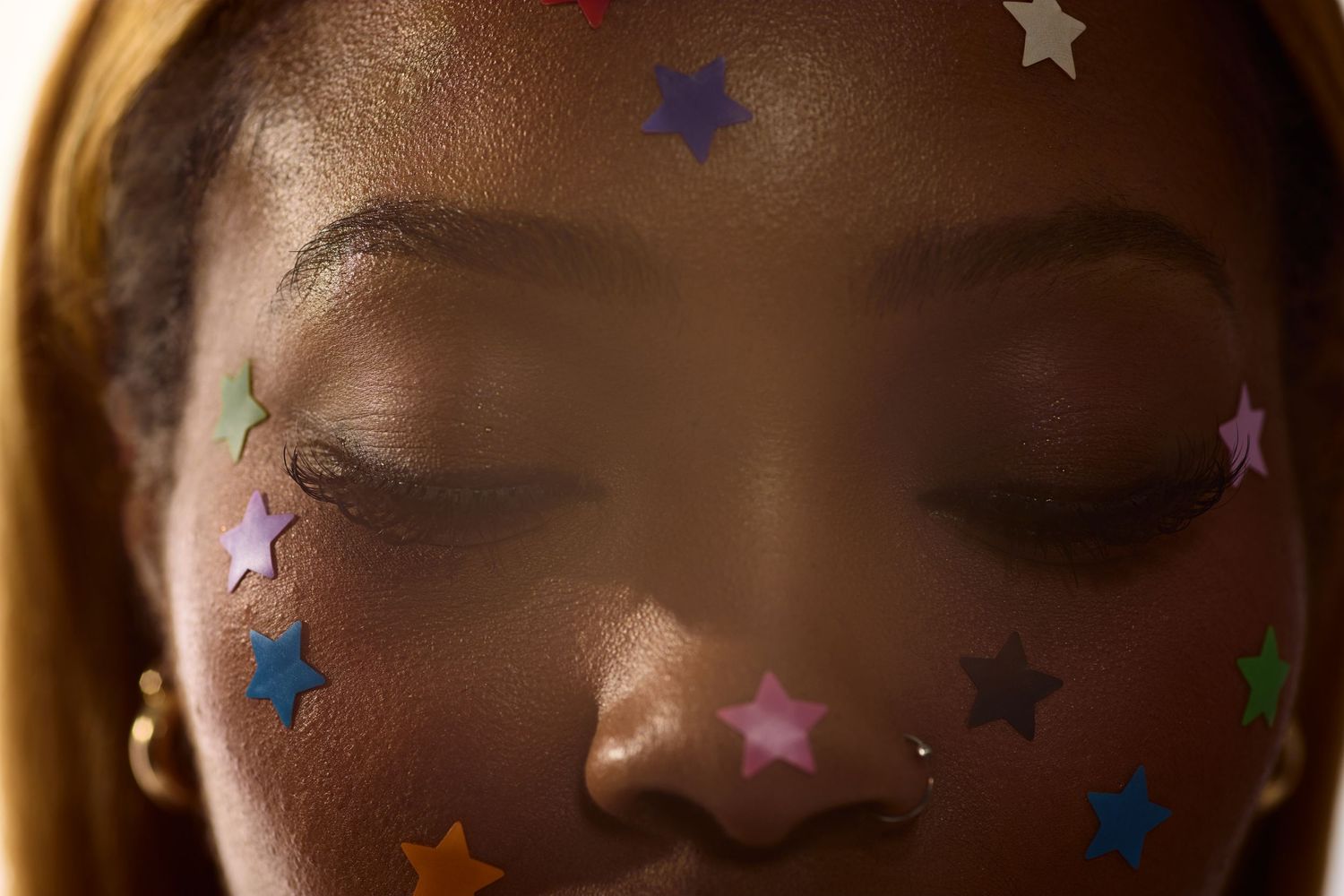 Extreme close-up of Black woman's face decorated with vibrant multicolored star-shaped stickers with eyes closed.