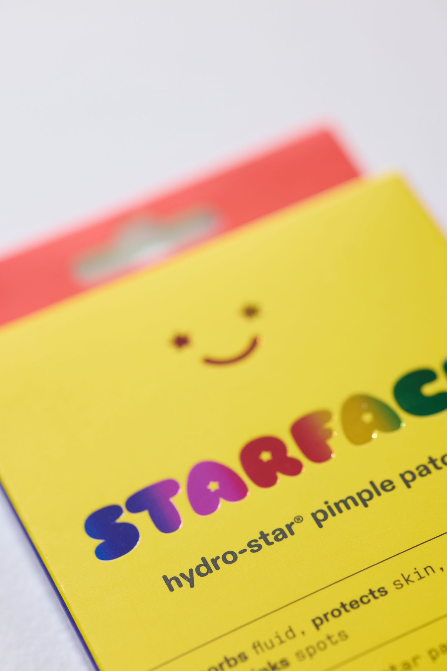 Close-up of Starface hydro-star pimple patch yellow packaging with rainbow logo and smiley face.