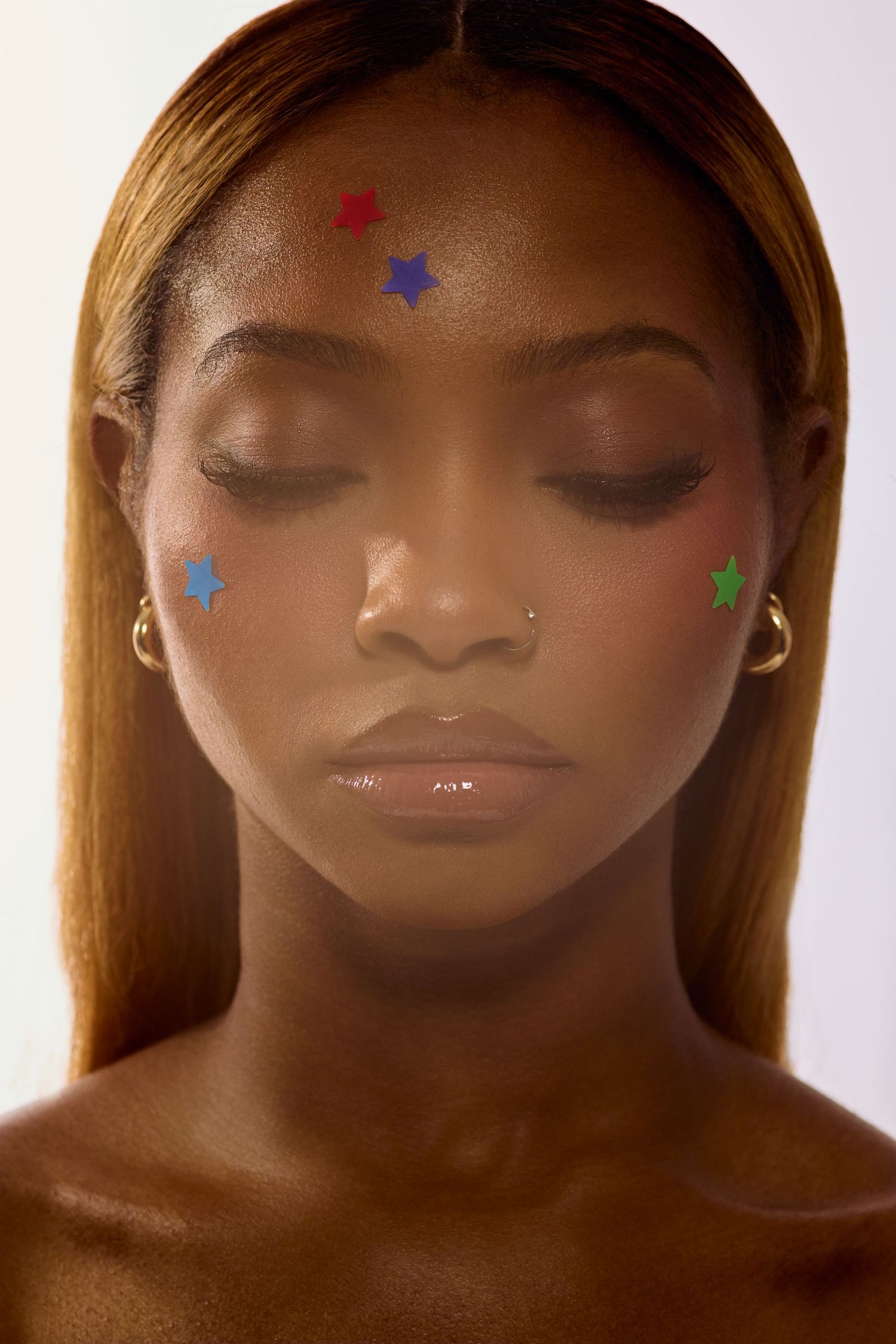 Beauty portrait of woman with straight hair and colorful star Starface patches on face, eyes closed.