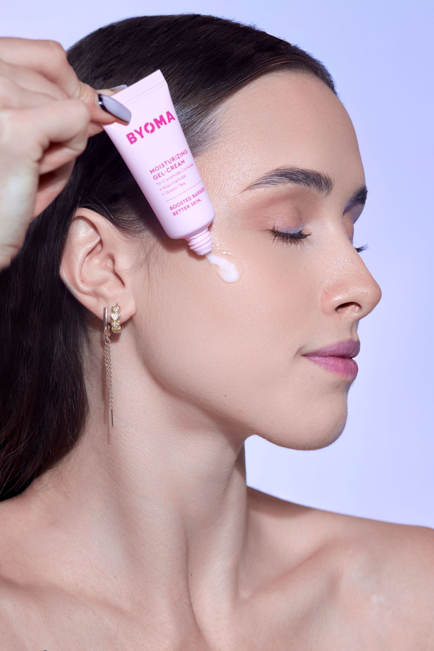 Woman applying BYOMA Moisturizing Gel-Cream to her cheek, showcasing the pink skincare tube product.