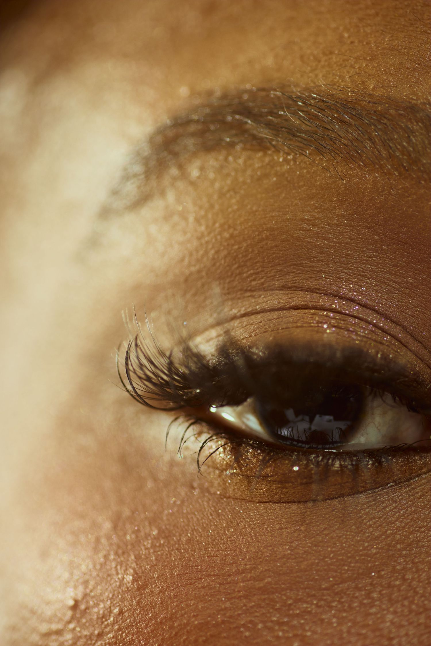 Macro close-up of a woman's eye with long lashes and golden shimmer makeup.