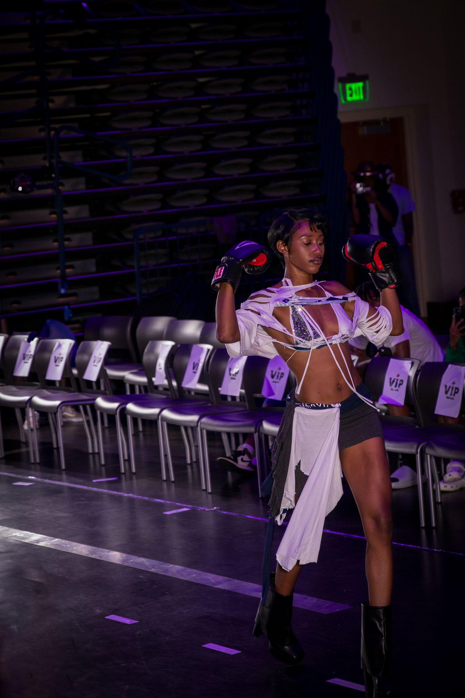 Model poses on runway wearing deconstructed white outfit with boxing gloves at edgy fashion show.