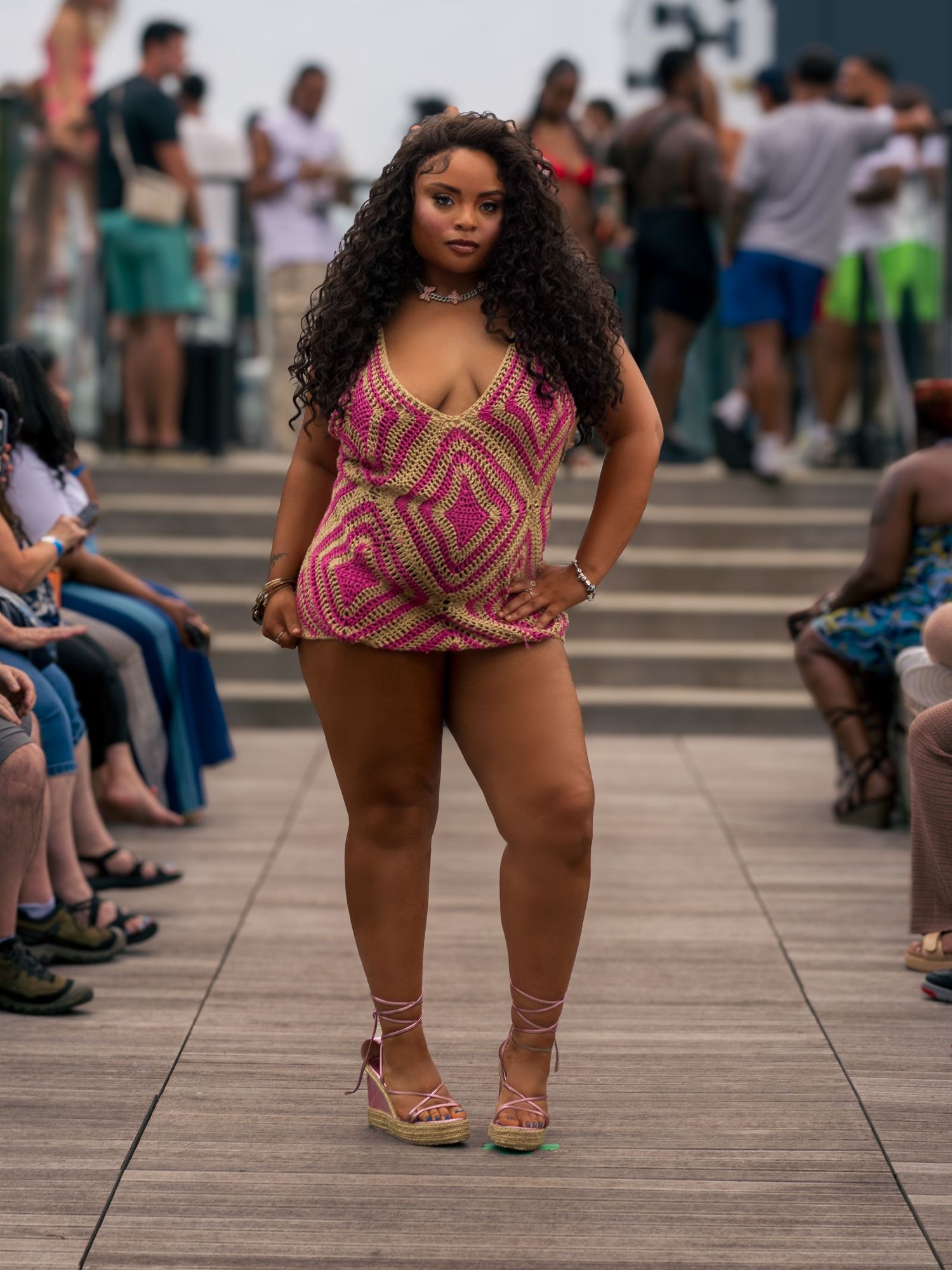Model in pink patterned mini dress poses confidently on outdoor fashion runway.