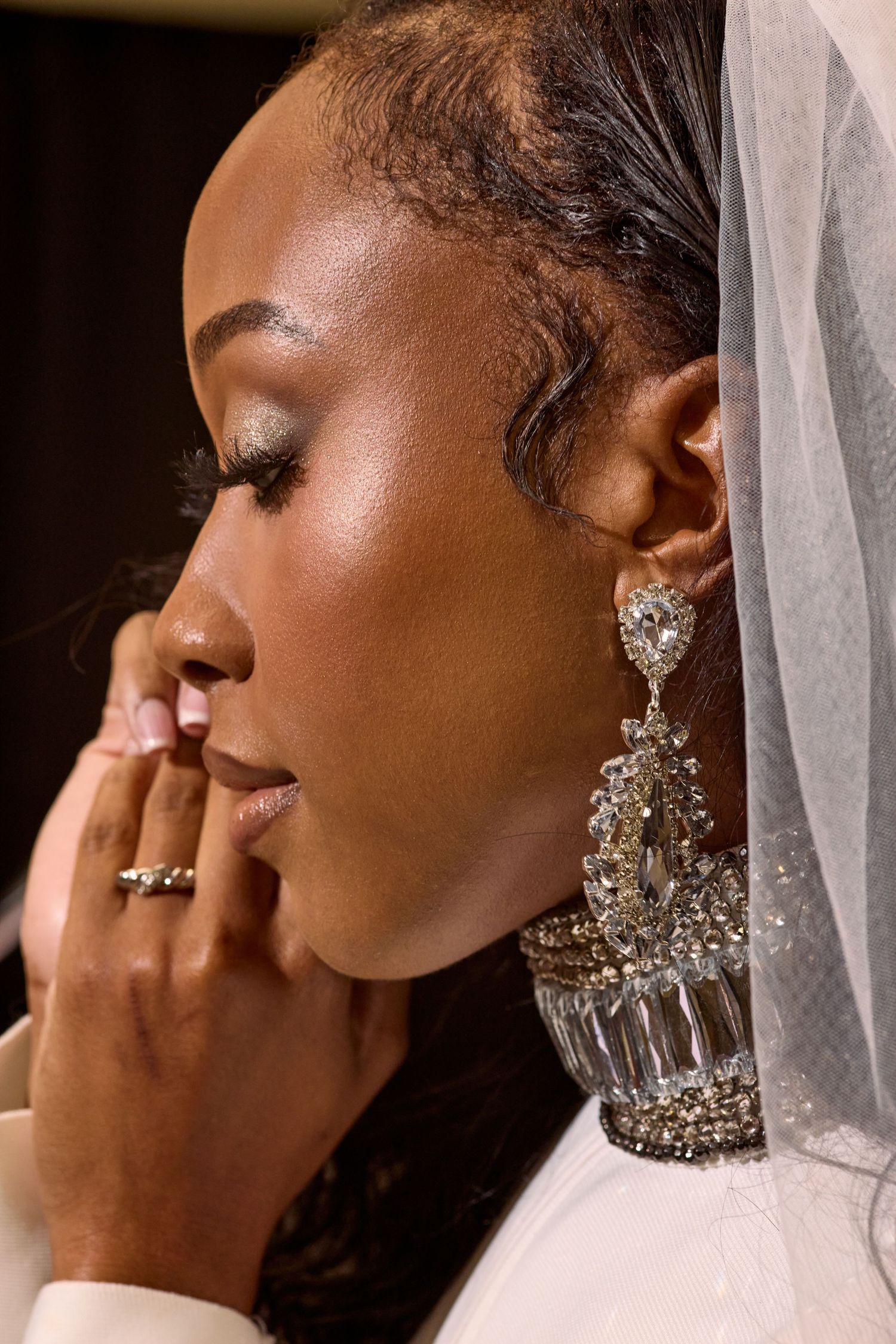 Close-up profile of Black bride wearing large crystal chandelier earrings and veil with diamond ring.