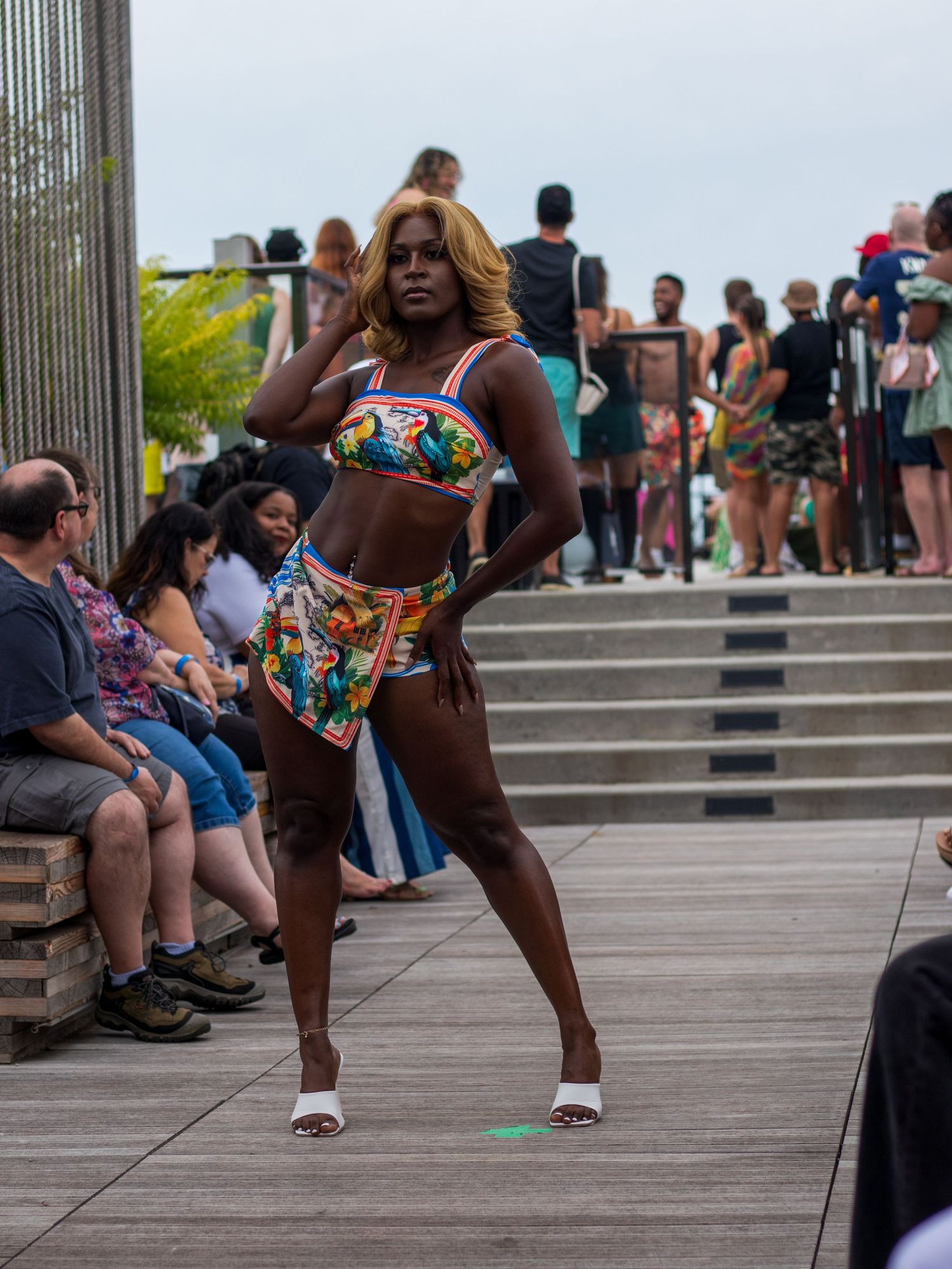Model in vibrant printed bikini with wrap accessory poses confidently on outdoor fashion runway.