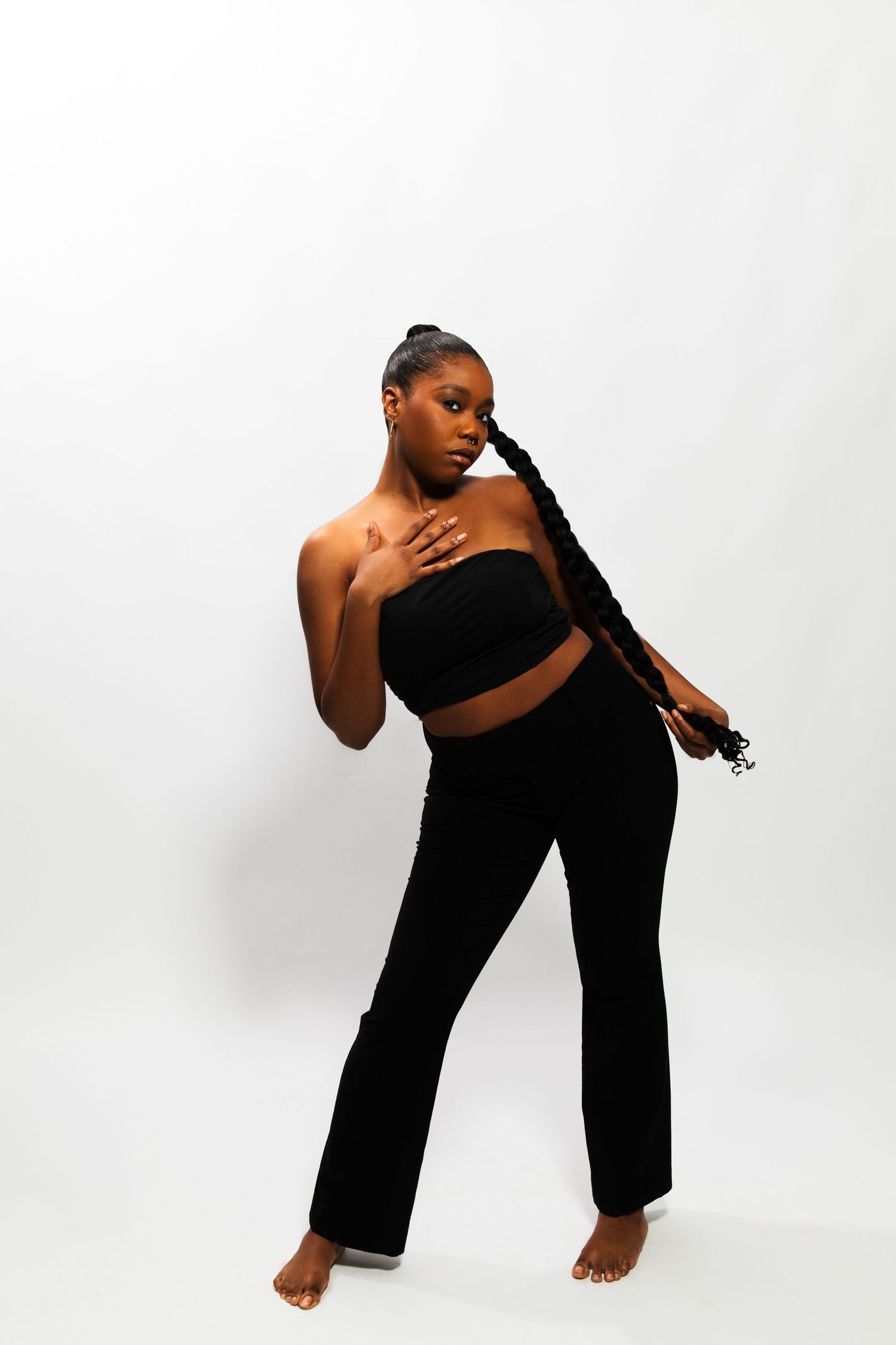 Black woman in black bandeau and flared pants posing with long braid draped over shoulder.