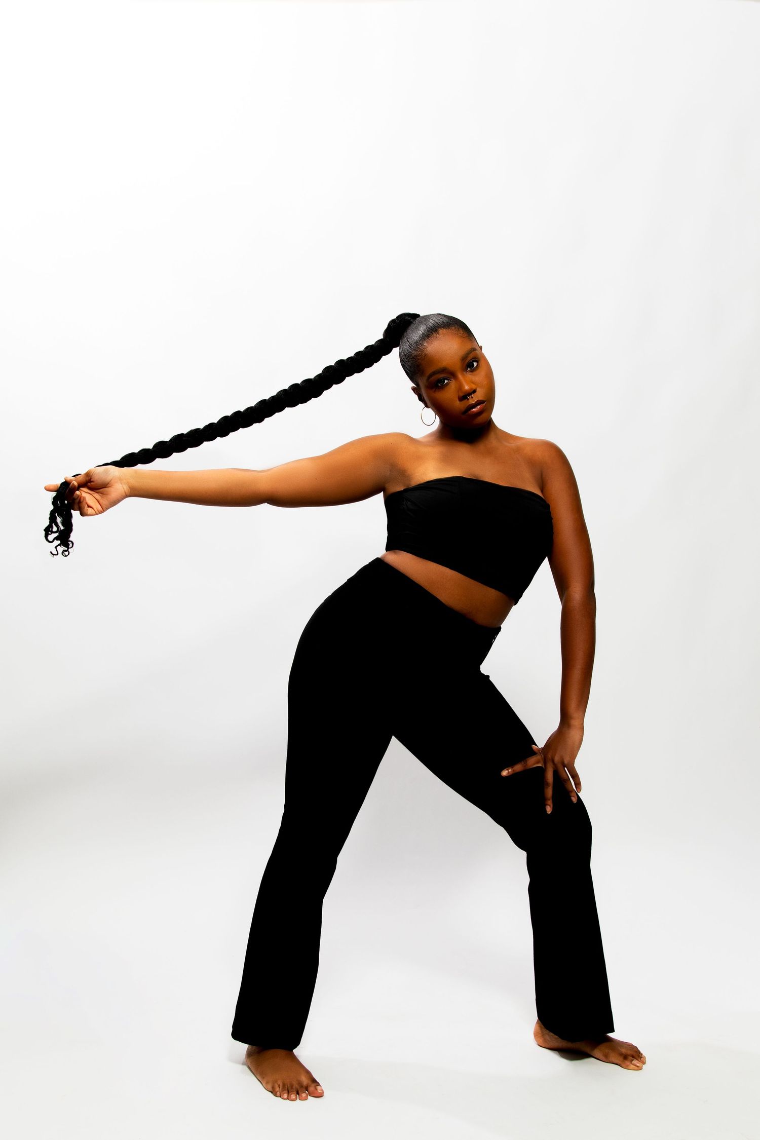Model in black crop top and flare pants posing with long braid.