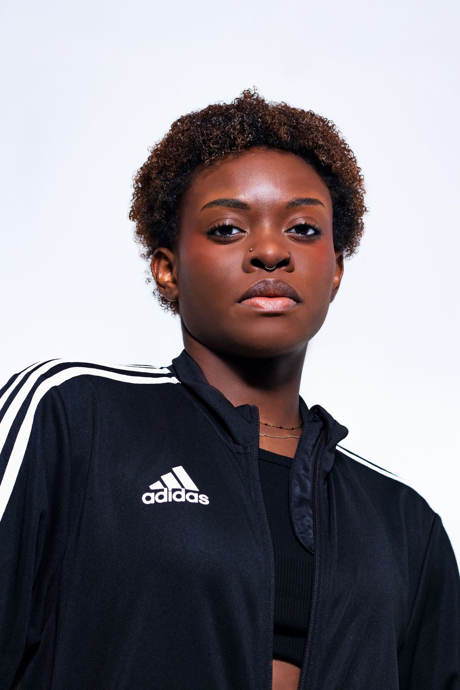 Young Black female athlete in black Adidas track jacket posing confidently against white background.
