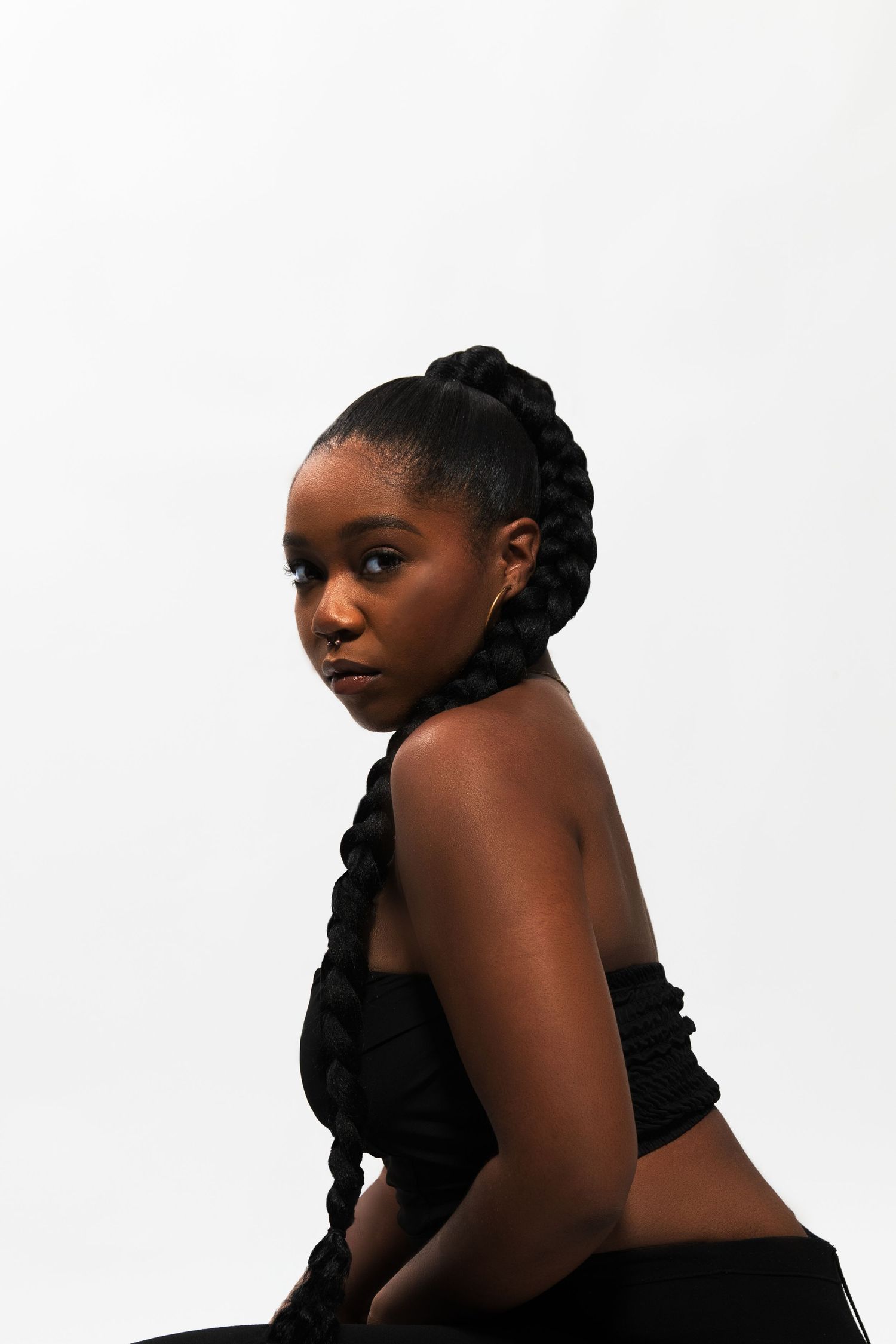 Side profile of Black woman in black crop top with thick braided updo against white background.