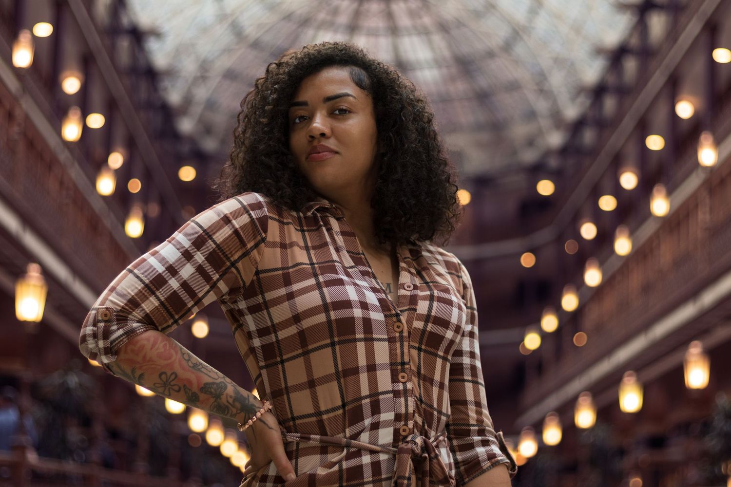 Woman in plaid dress posing under glass dome with lights.