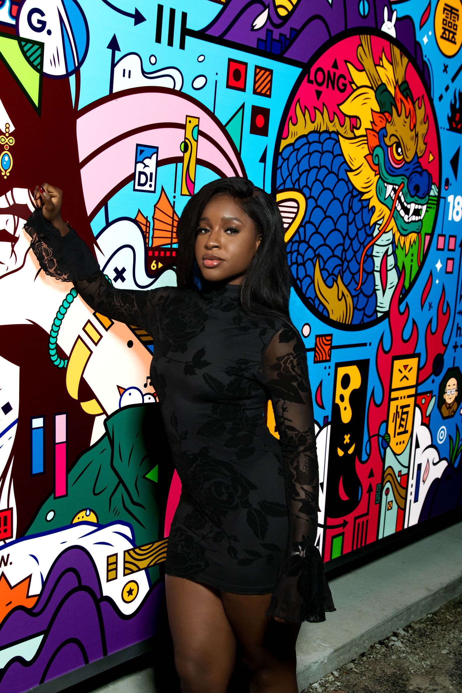 Woman in black lace dress poses before vibrant colorful graffiti mural.