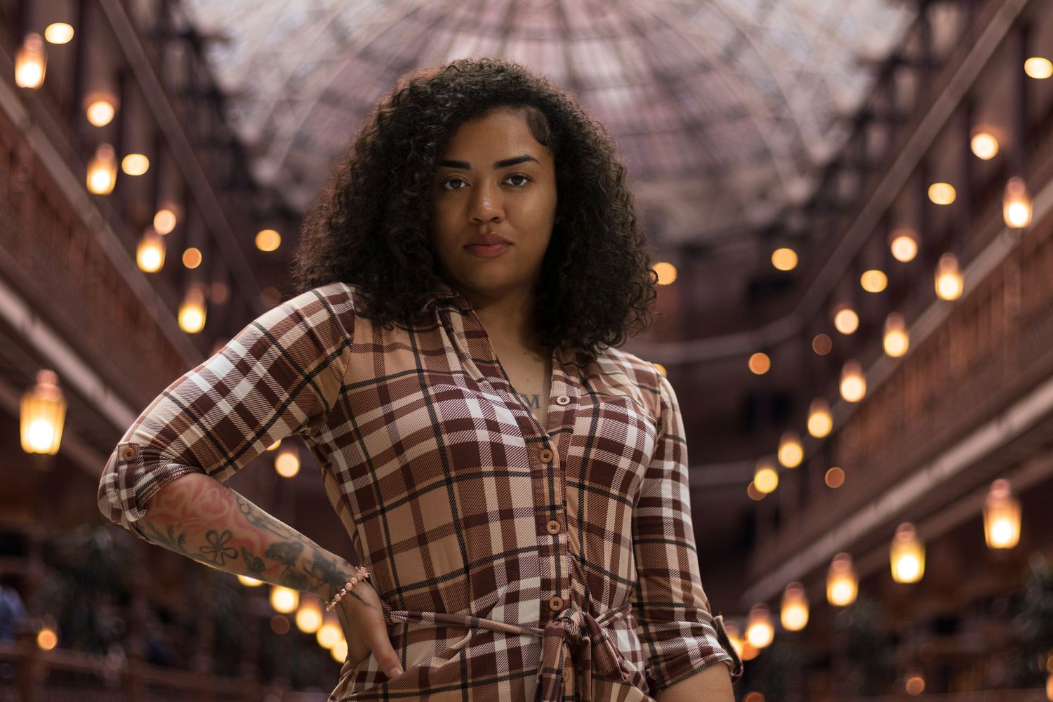 Woman in plaid dress standing in ornate arcade with lights.