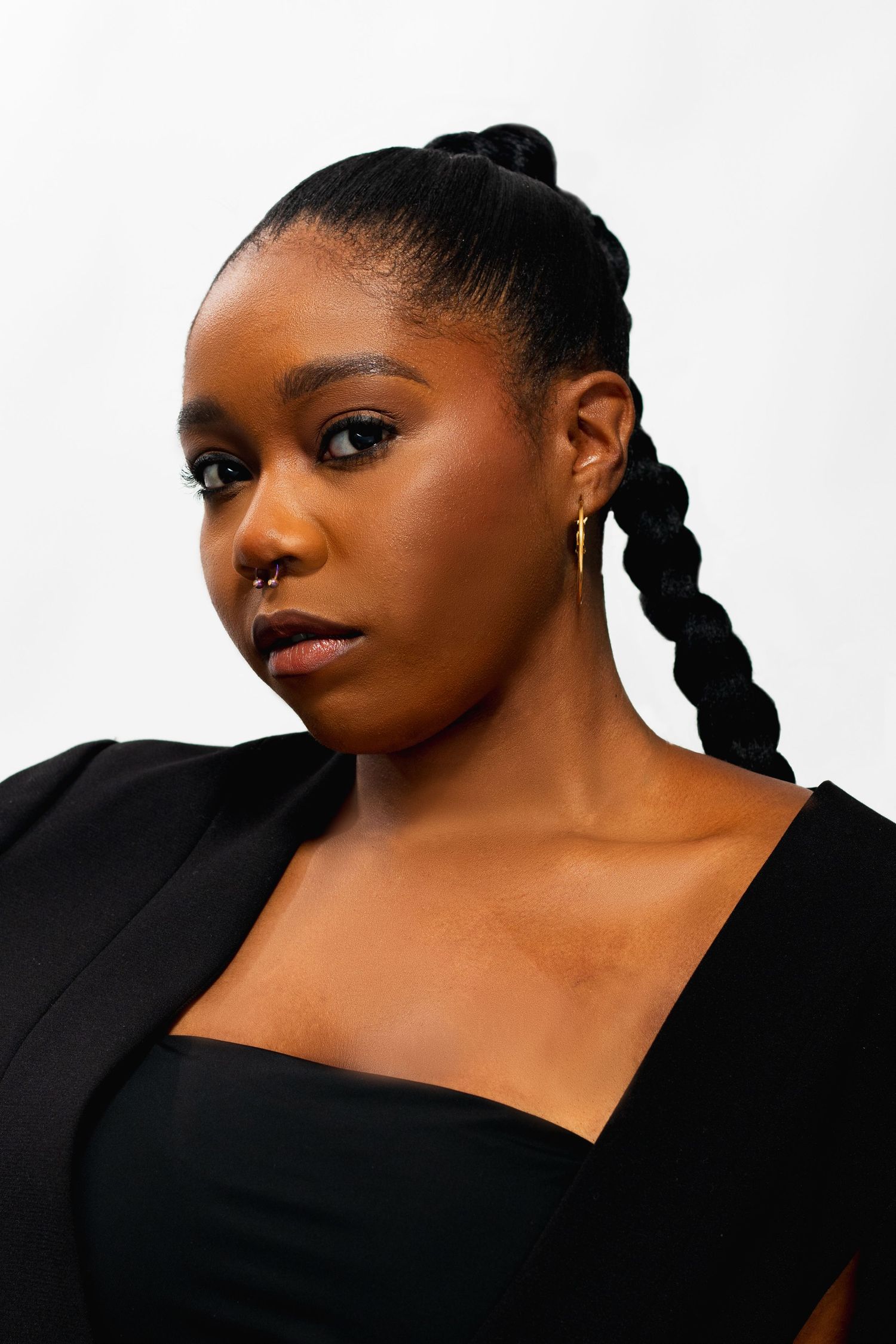 Close-up portrait of Black woman with braided updo wearing black blazer and gold hoop earring.