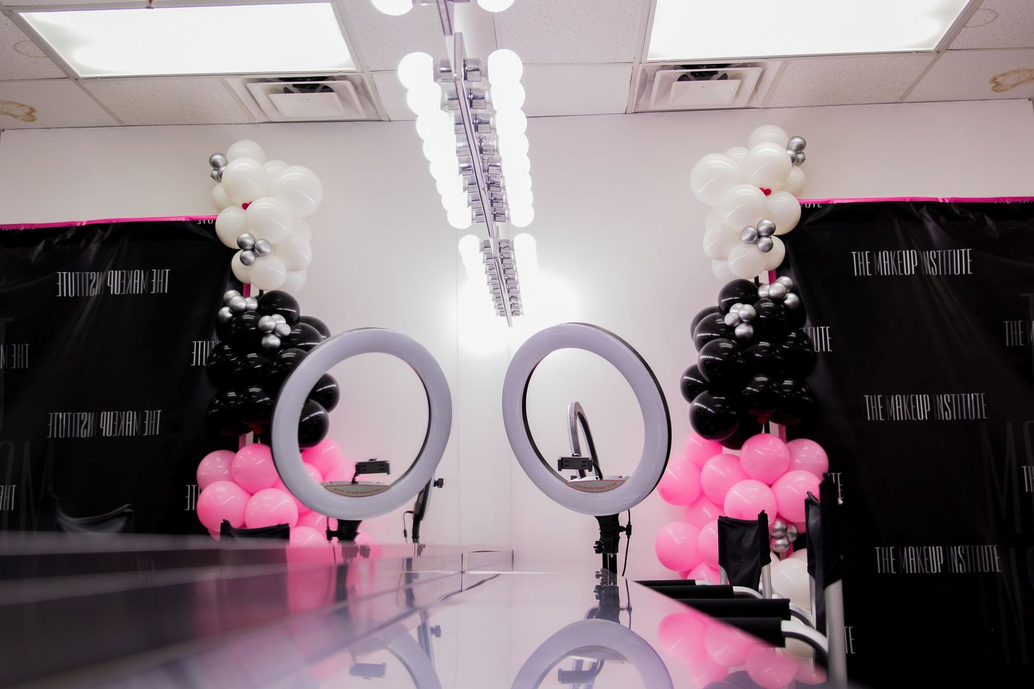 Professional makeup studio setup with ring lights and black, white, and pink balloon decorations.