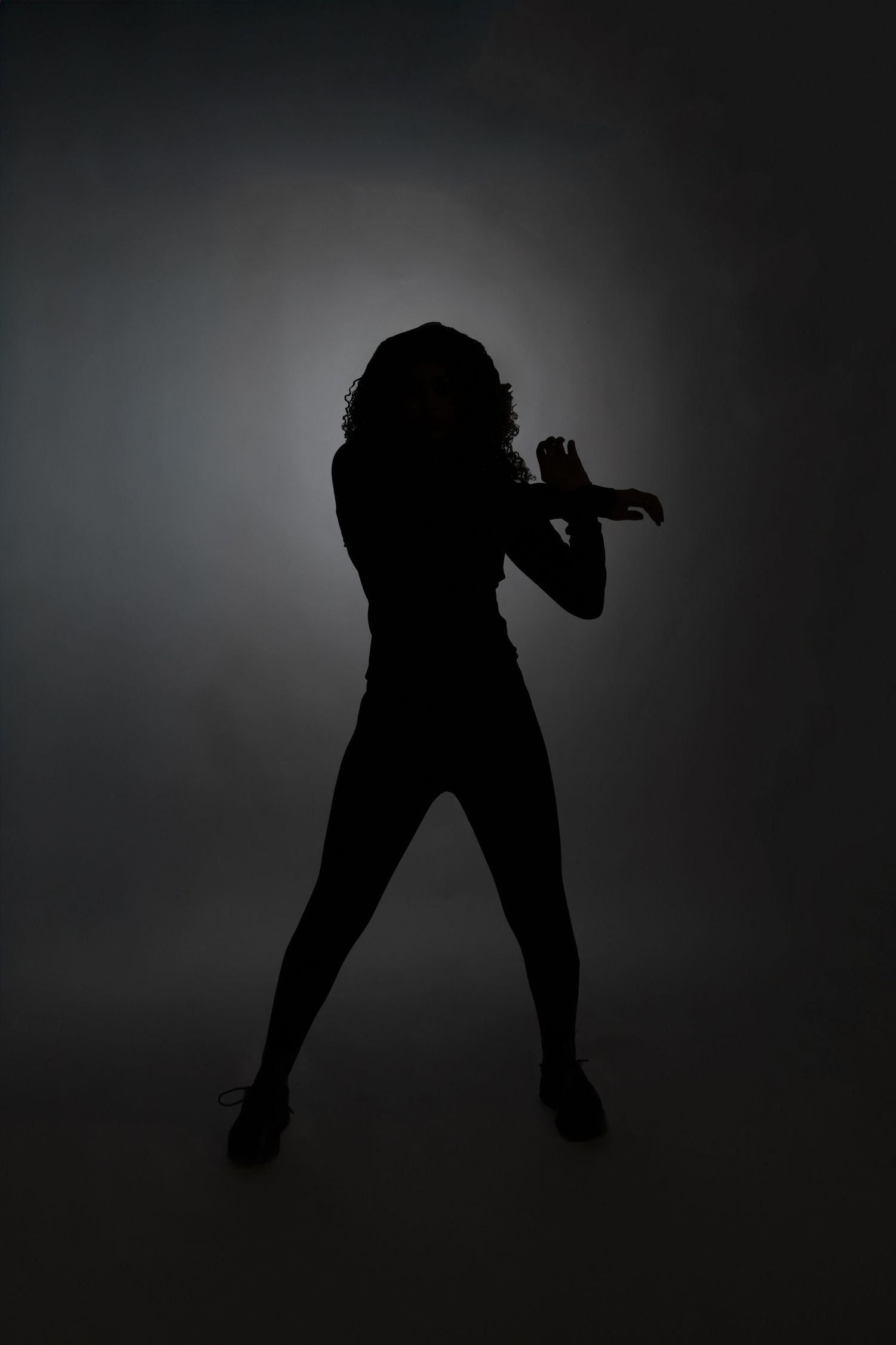 Dramatic silhouette of a woman dancing in a fighting pose against a dark moody studio background.