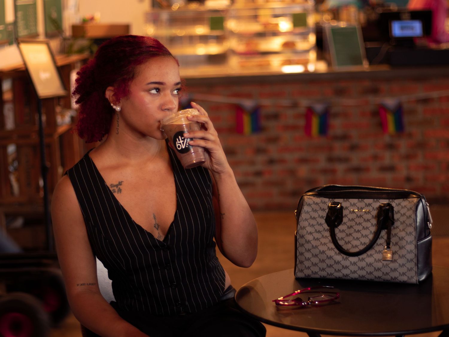 Woman sipping iced drink beside checkered designer handbag in warmly lit cafe.
