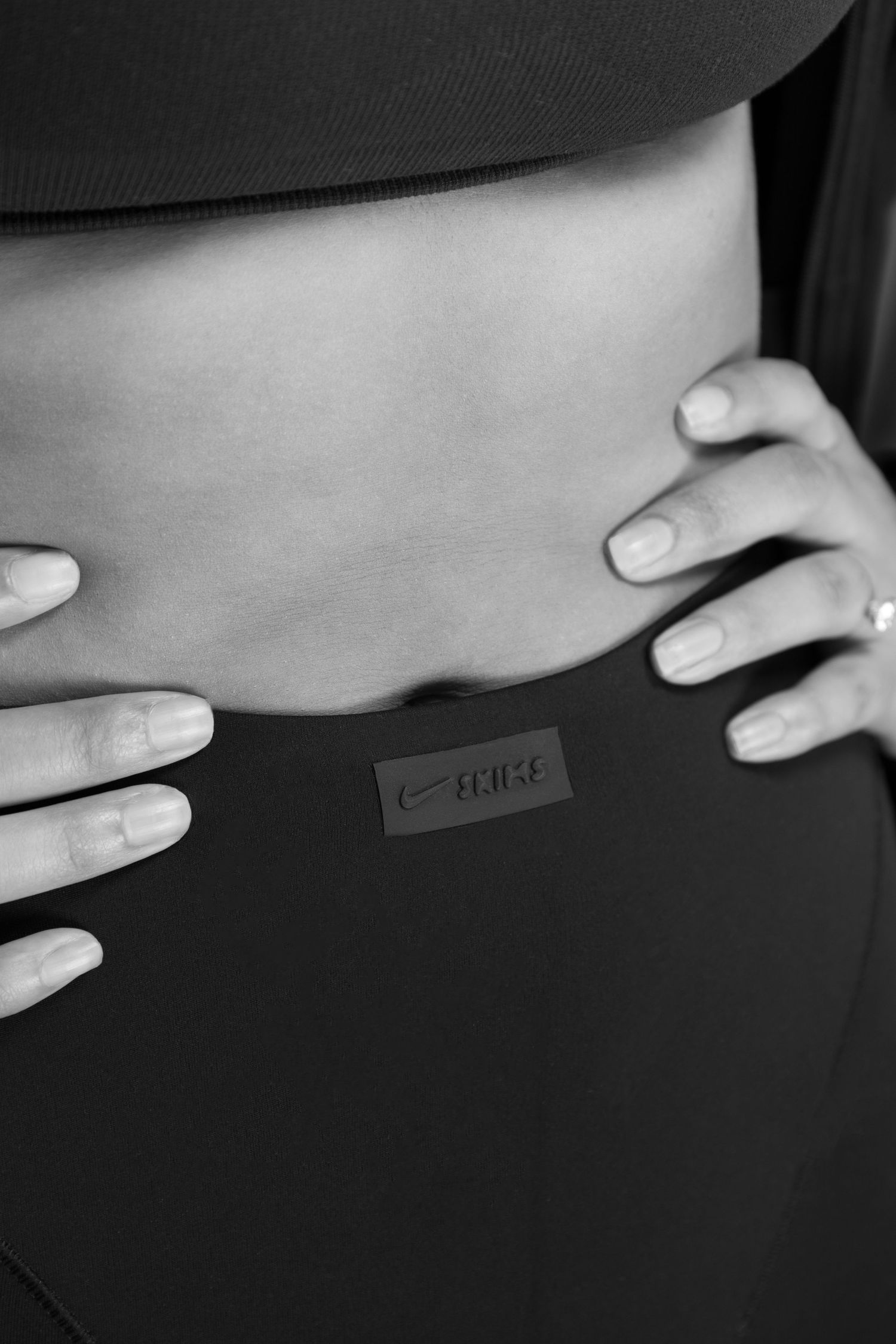 Close-up black and white photo of a woman's midsection wearing Nike leggings with hands on hips.