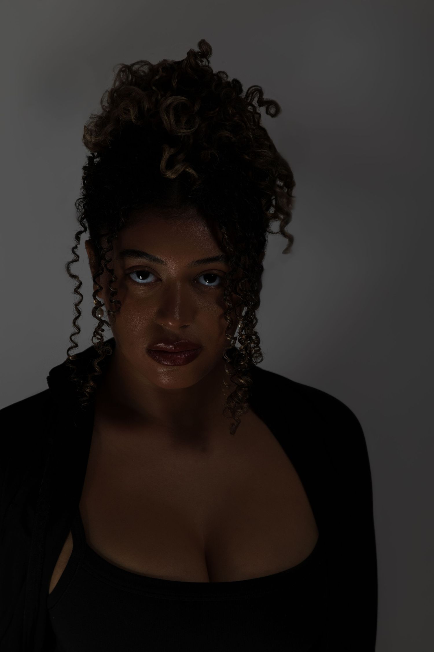 A woman with voluminous curly updo hairstyle poses in a black top against a dark gray background.