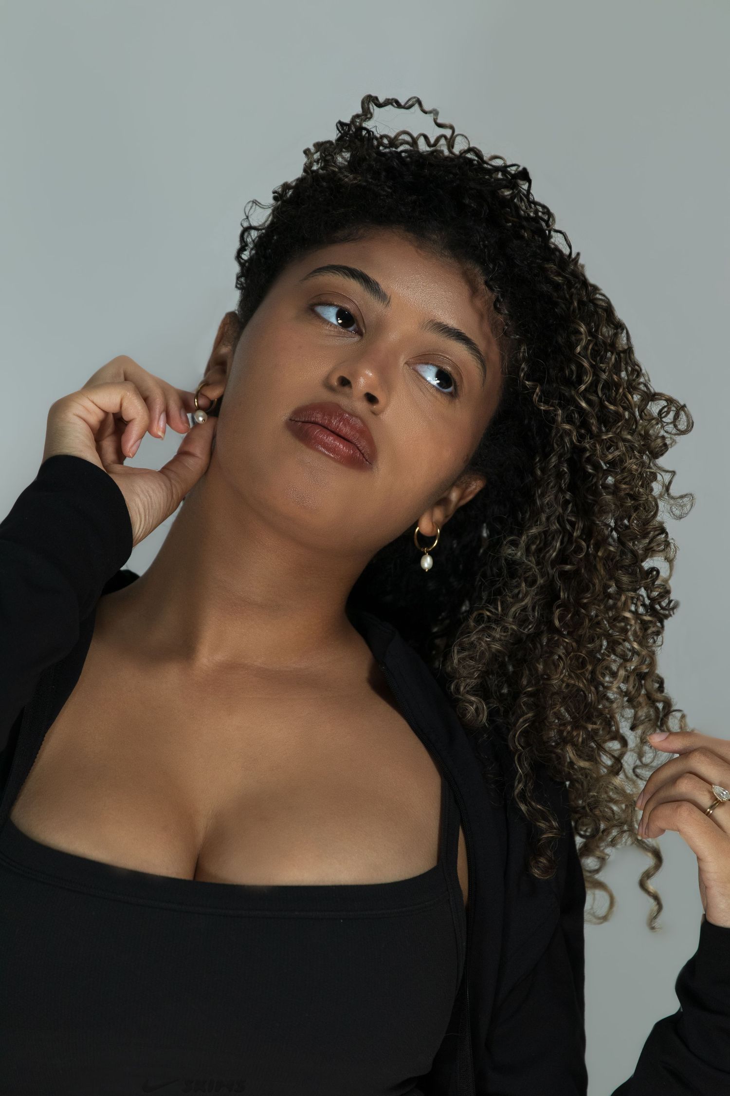Portrait of a curly-haired woman in black outfit with gold earrings looking upward in studio.