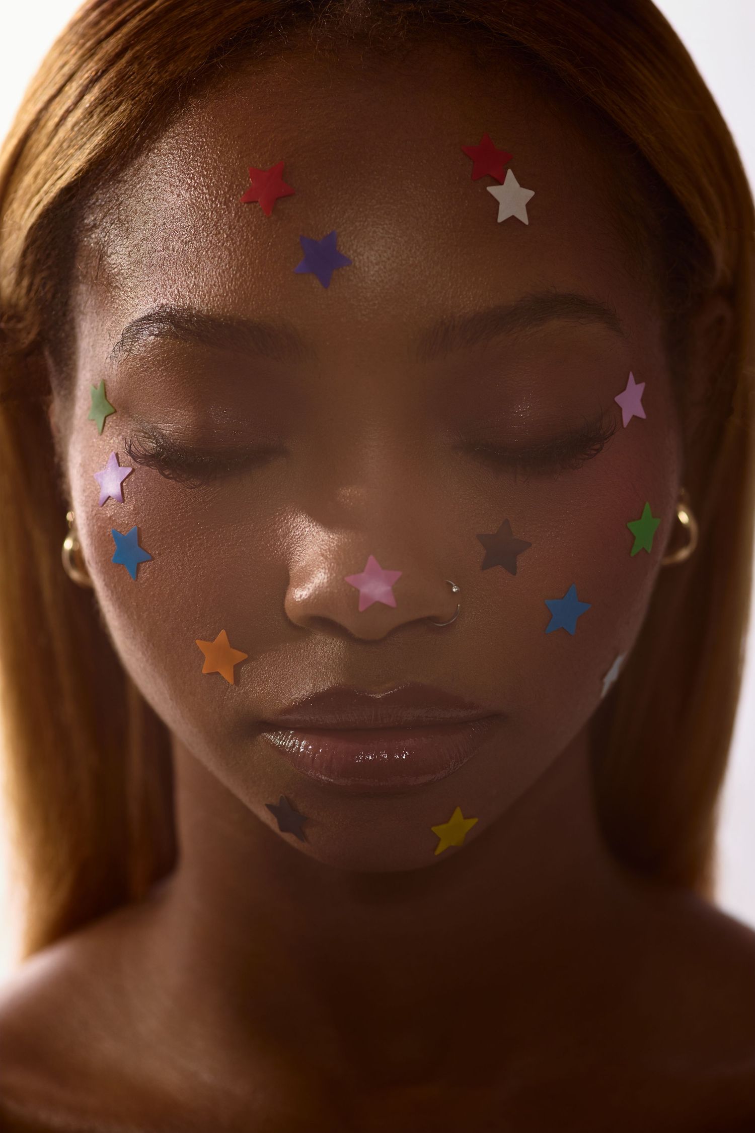 Portrait of Black woman with eyes closed covered in multicolored star stickers on face and forehead.
