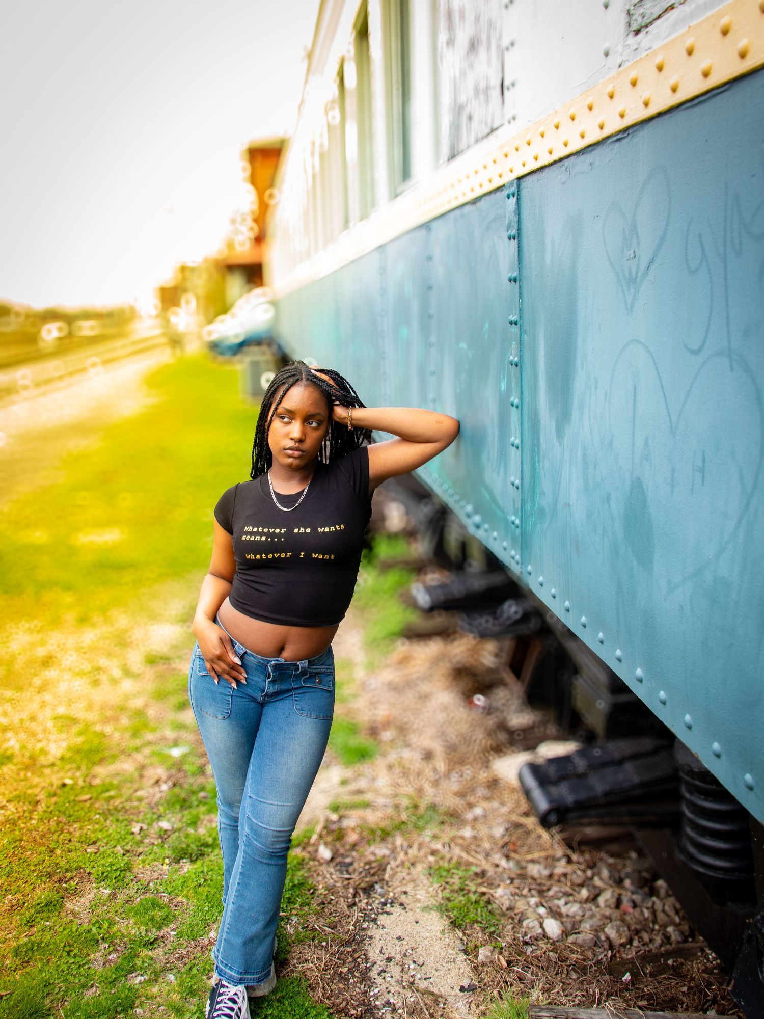 Young woman in black crop top and jeans leaning against a vintage train car.