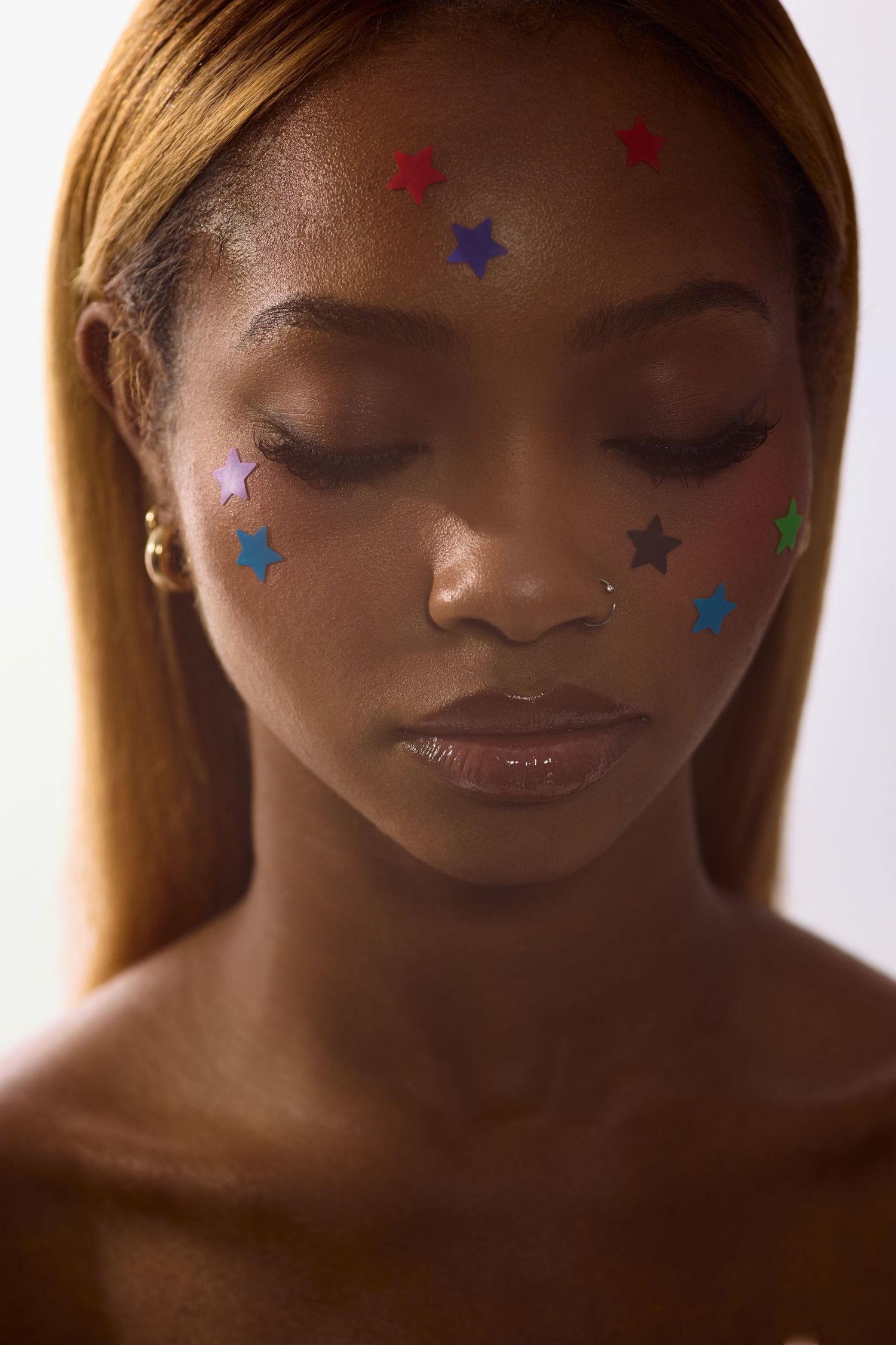 Close-up portrait of Black woman with closed eyes and multicolored star stickers decorating her face.