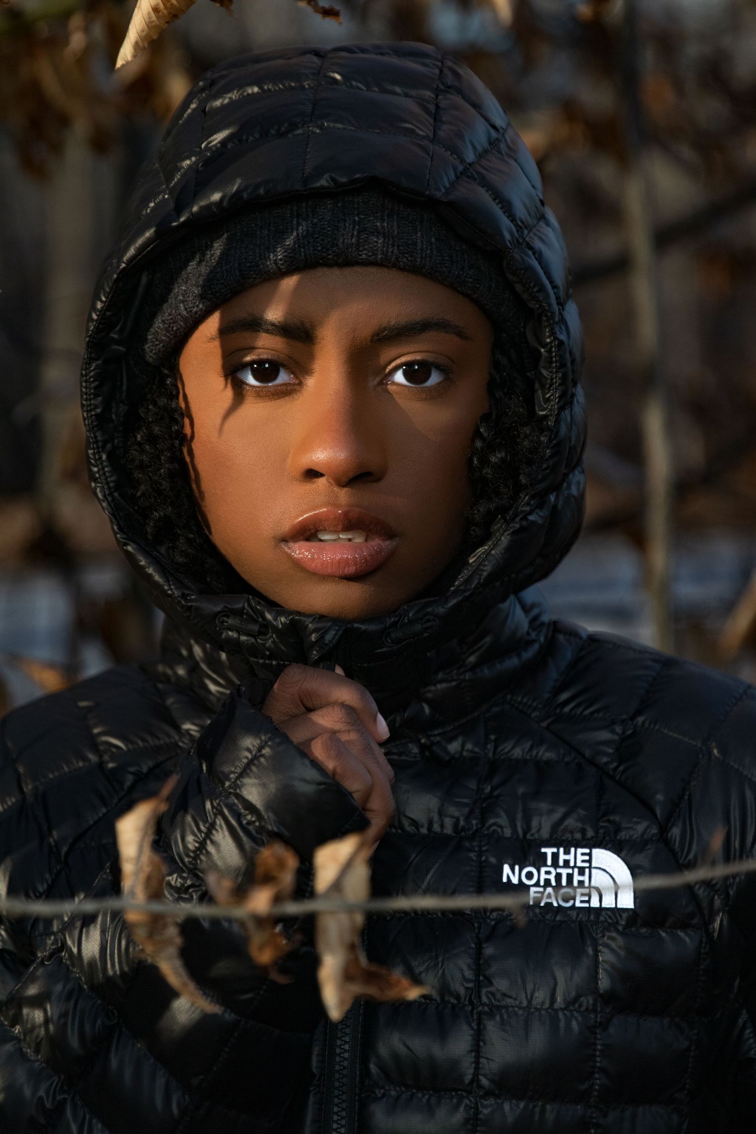 Young person in black North Face hooded jacket holding wire fence in autumn forest.