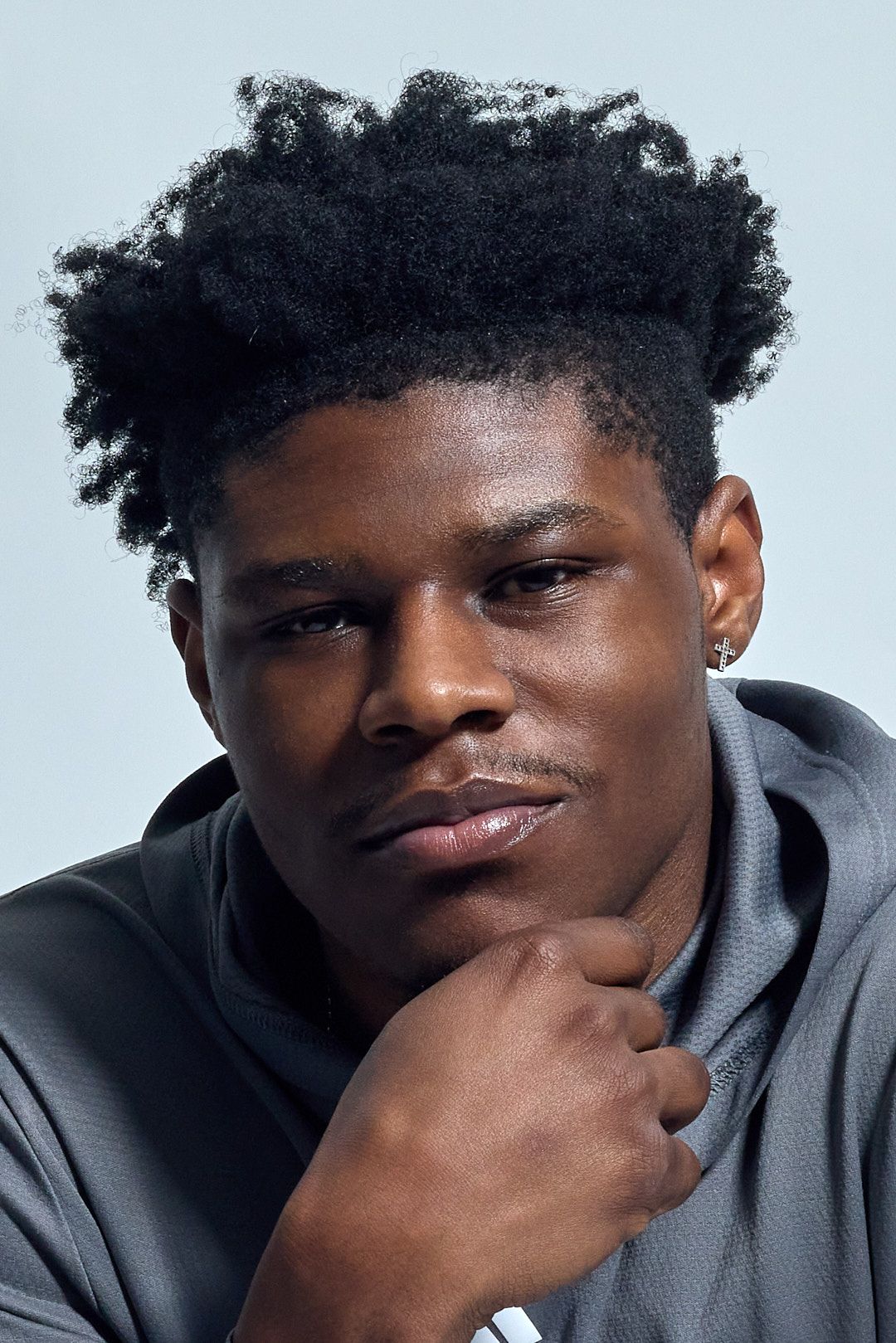 Young Black man with natural afro hairstyle posing confidently against a light background.