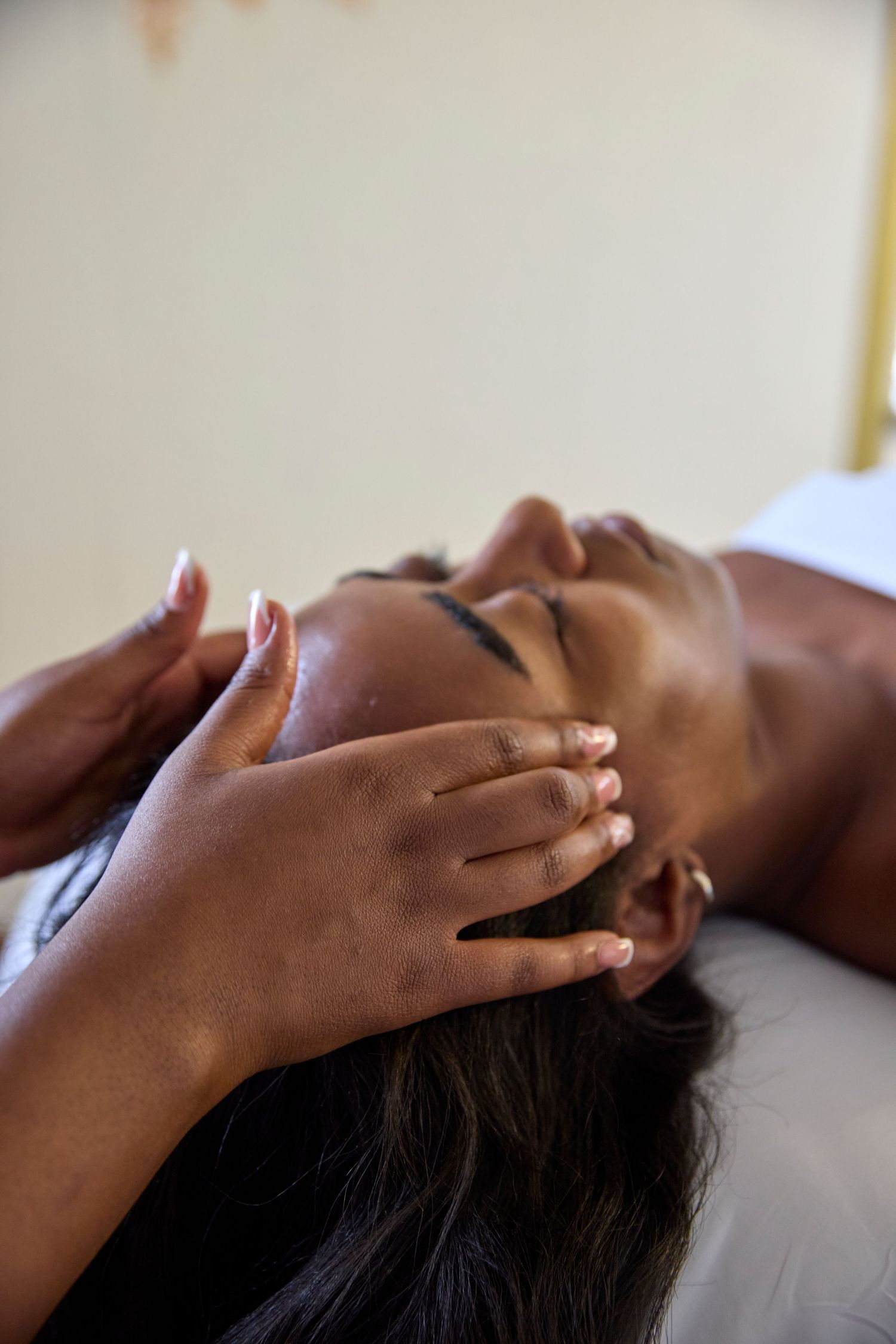 A woman receiving a relaxing facial massage at a spa, with therapist hands gently pressing on her face.