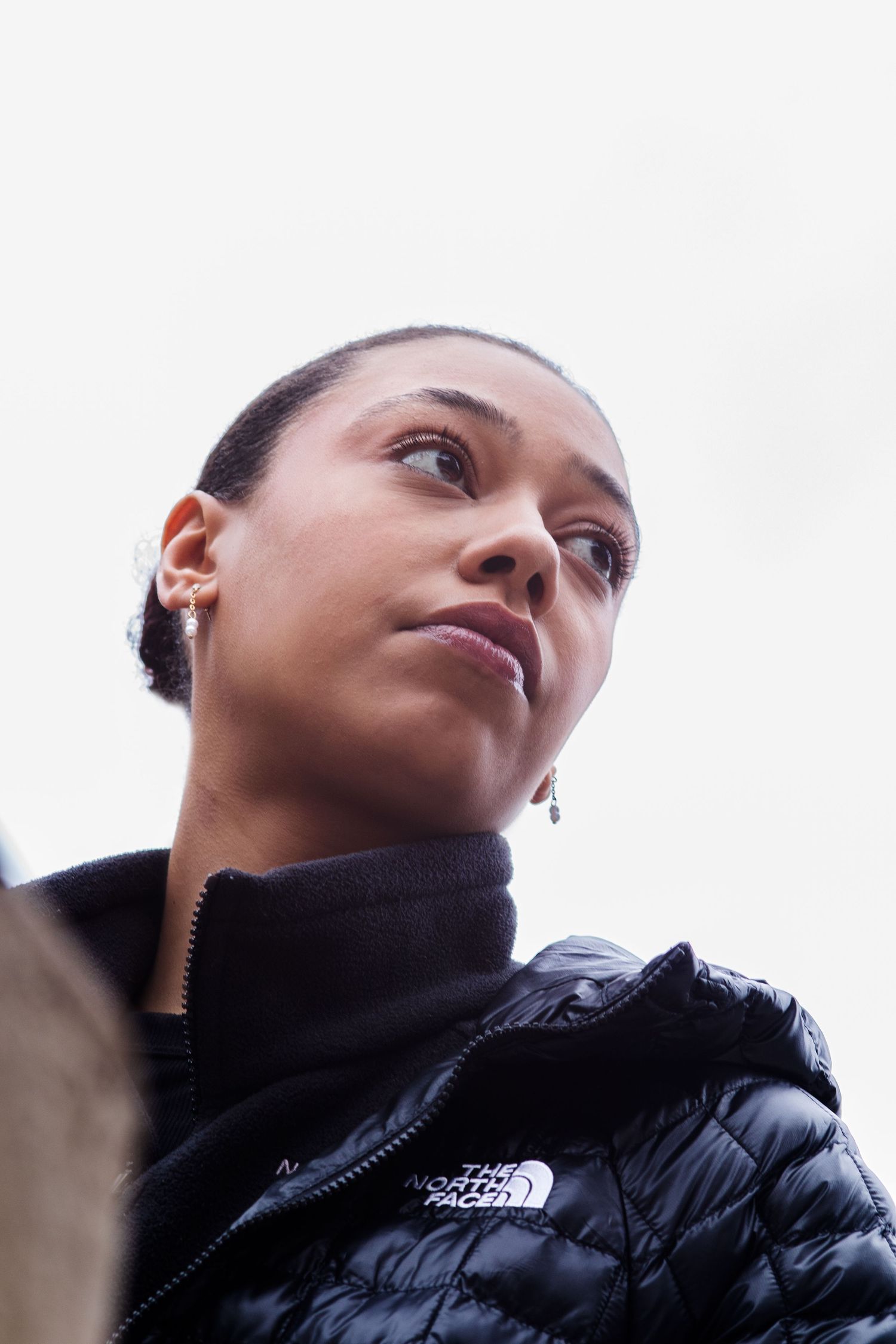 Low angle portrait of woman in black North Face jacket looking upward outdoors.