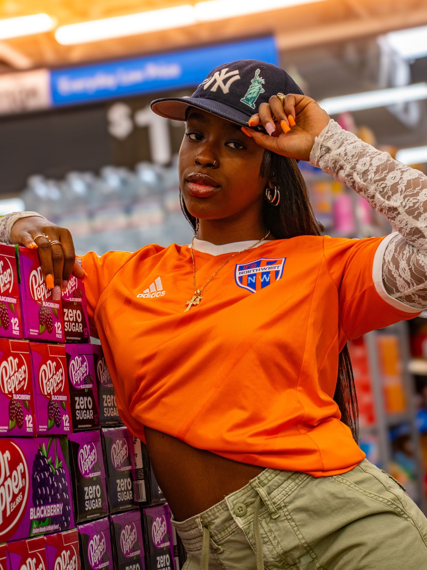 Woman in orange Adidas jersey and NY Yankees cap posing in a store aisle with Dr Pepper cases.