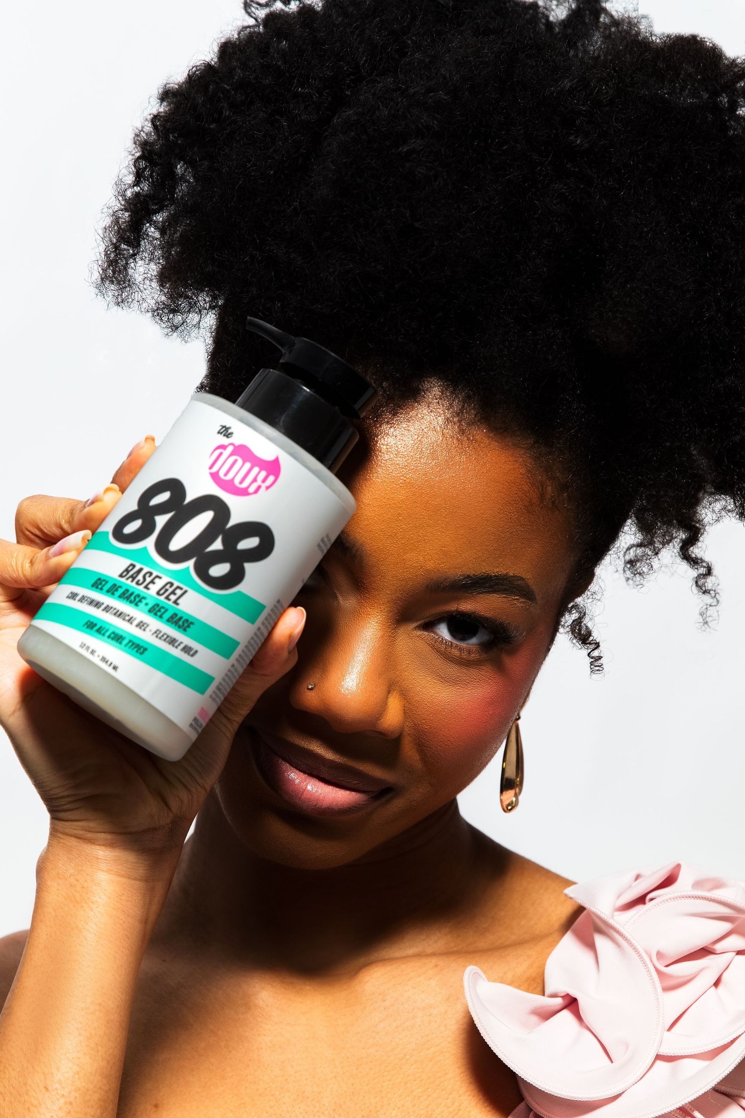 Woman holding The Doux 808 Base Gel jar against her cheek, showcasing natural afro hairstyle.