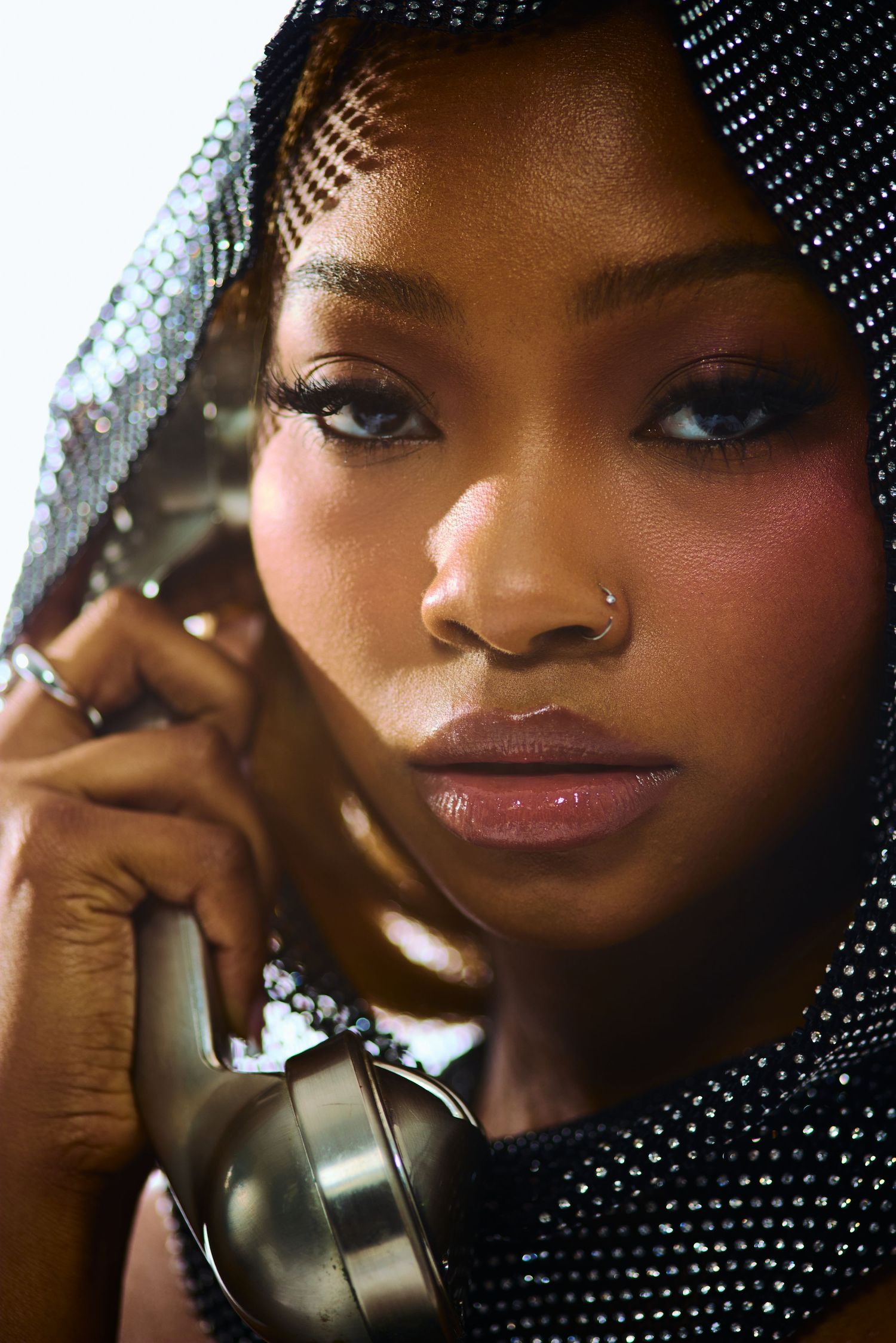 Portrait of a Black woman in a rhinestone hood holding a vintage silver telephone receiver to her ear.